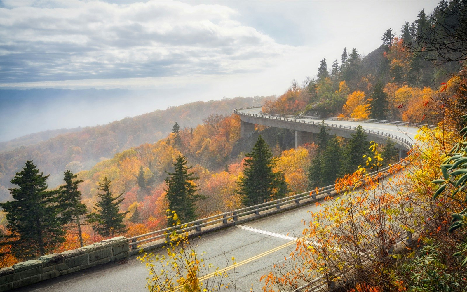 A viaduct along the Blue Ridge Parkway cuts through a forest turning various shades of yellow and orange