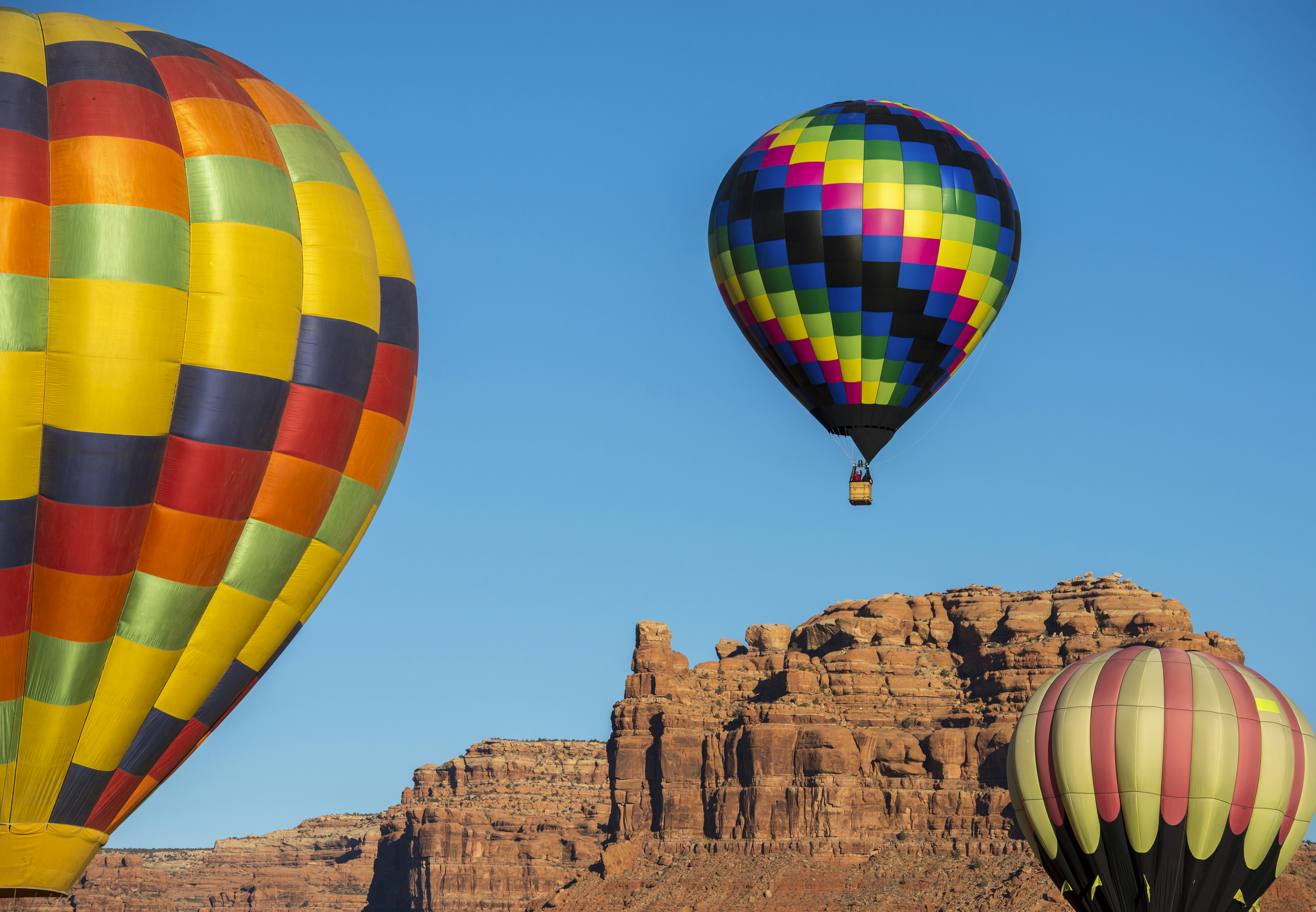 A trio of brightly colored hot air balloons soar around The Valley of the Gods during the Bluff International Balloon Festival.