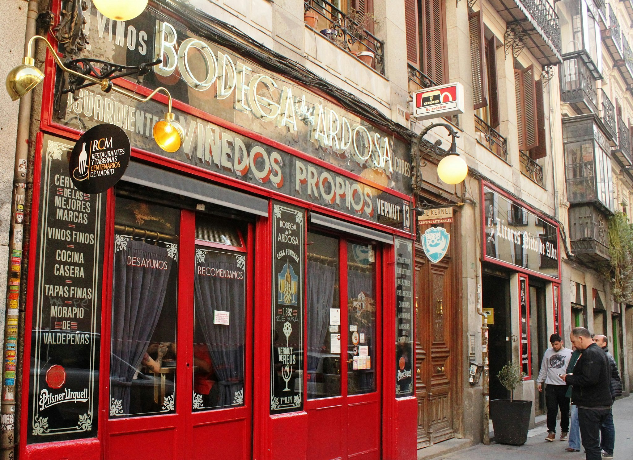 The bright red-painted facade of Bodega Ardosa, with old-fashioned signs announcing the bar's wares and mauve curtains hanging in the windows.