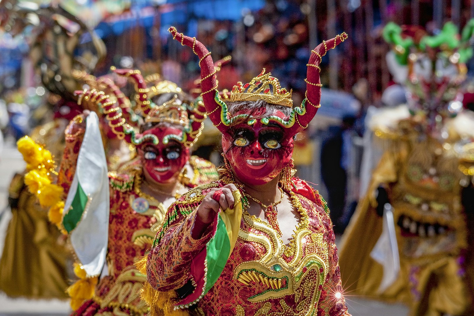 A line of dancers in red devil masks and elaborately sewn red and gold costumes walk through the streets during Carnival in Oruro, Bolivia