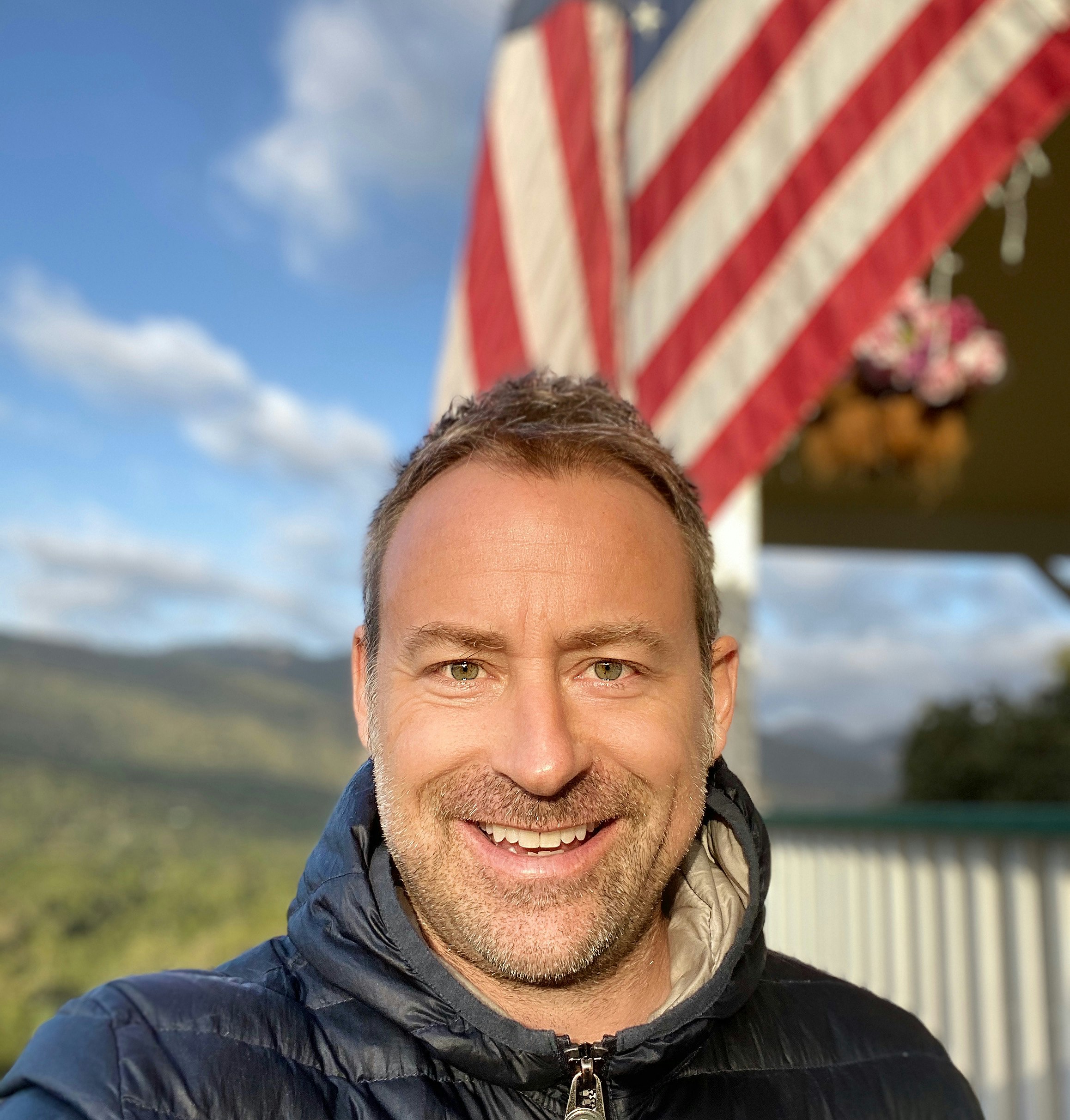 Writer Kevin Raub stands in front of an American-flag-draped structure and hilly scenery.
