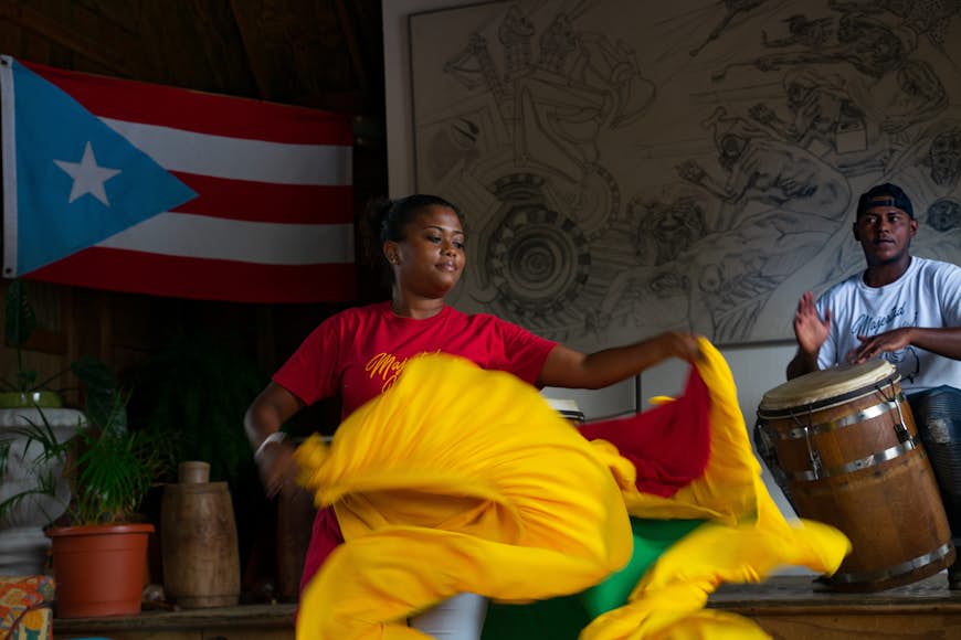 En kvinna snurrar på sin färgglada kjol mot en man som spelar trumma i bakgrunden;  Hållbart Puerto Rico 