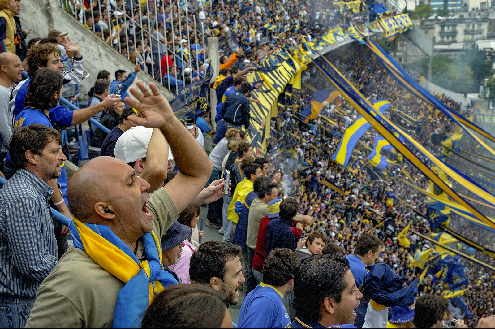 Fans dressed in blue and yellow cheering for their team at La Bombonera Stadium in Buenos Aires, Argentina