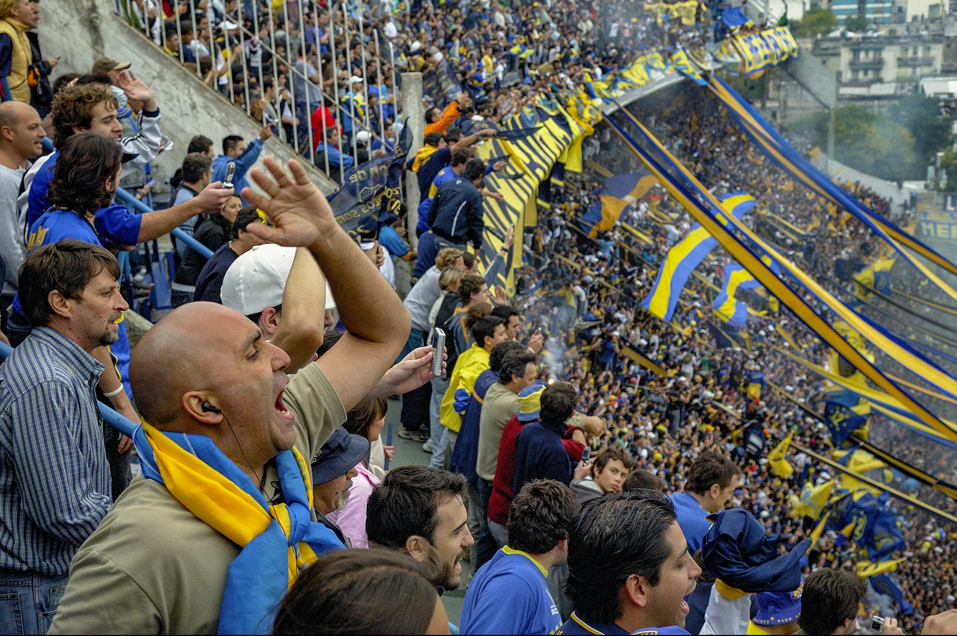 Fans dressed in blue and yellow cheering for their team at La Bombonera Stadium in Buenos Aires, Argentina