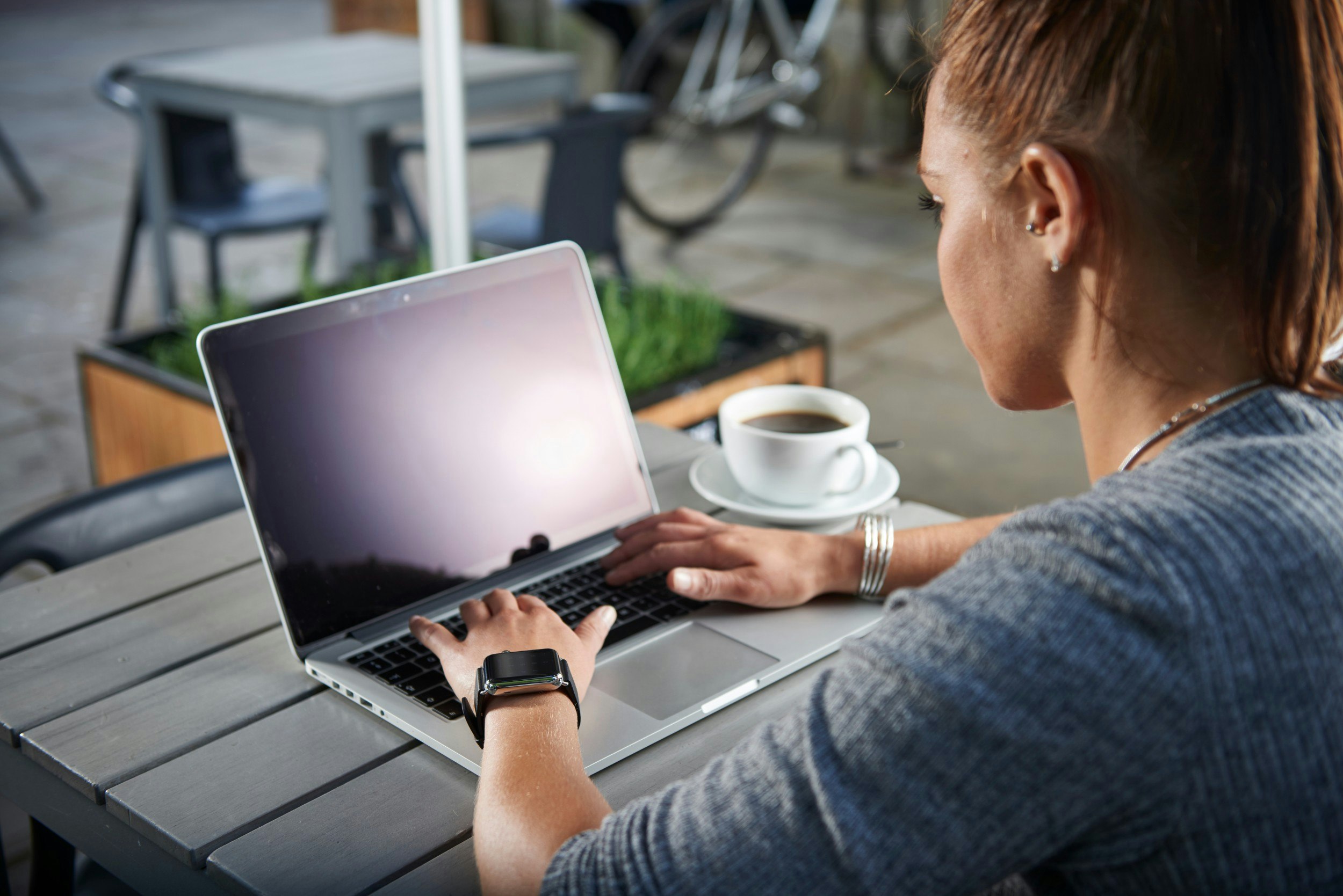 A woman wearing an Apple Watch on a laptop sitting outside a cafe