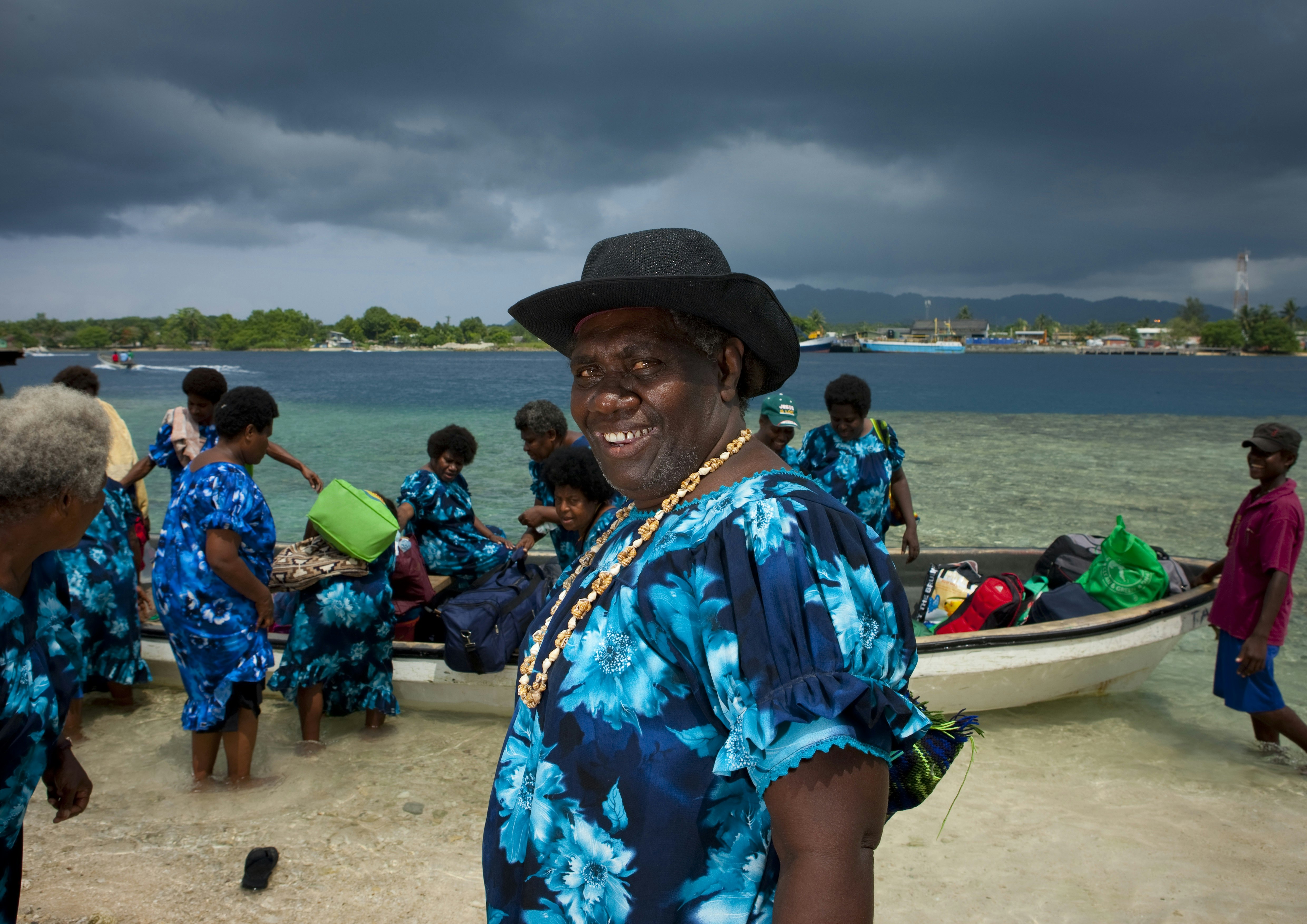 Beach scene in Bougainville with men and women in colourful shirts getting into boats