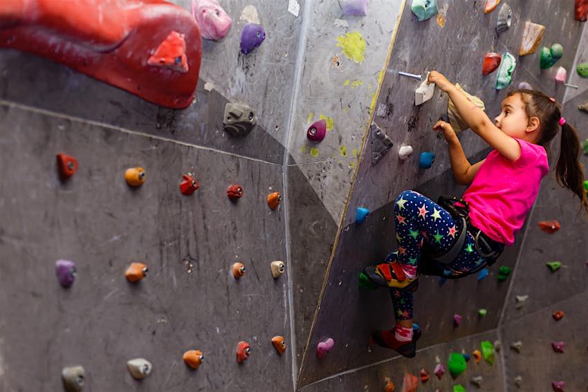 A young girl climbs on a bouldering wall in a climbing gym; kids outdoor adventures