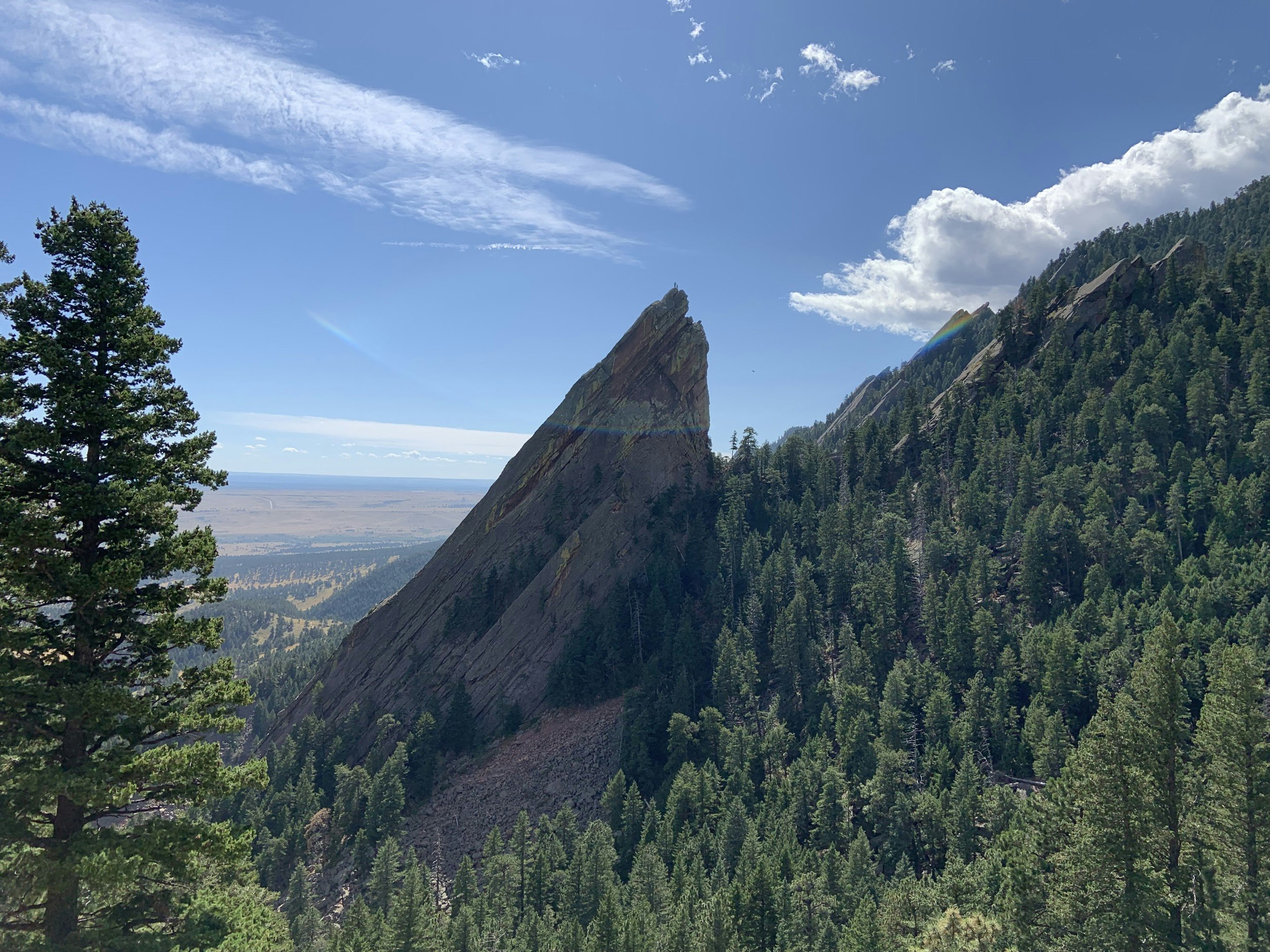 Looking across a valley at a jagged spire of rock with some climbers on top of it; Hiking in Boulder, Colorado