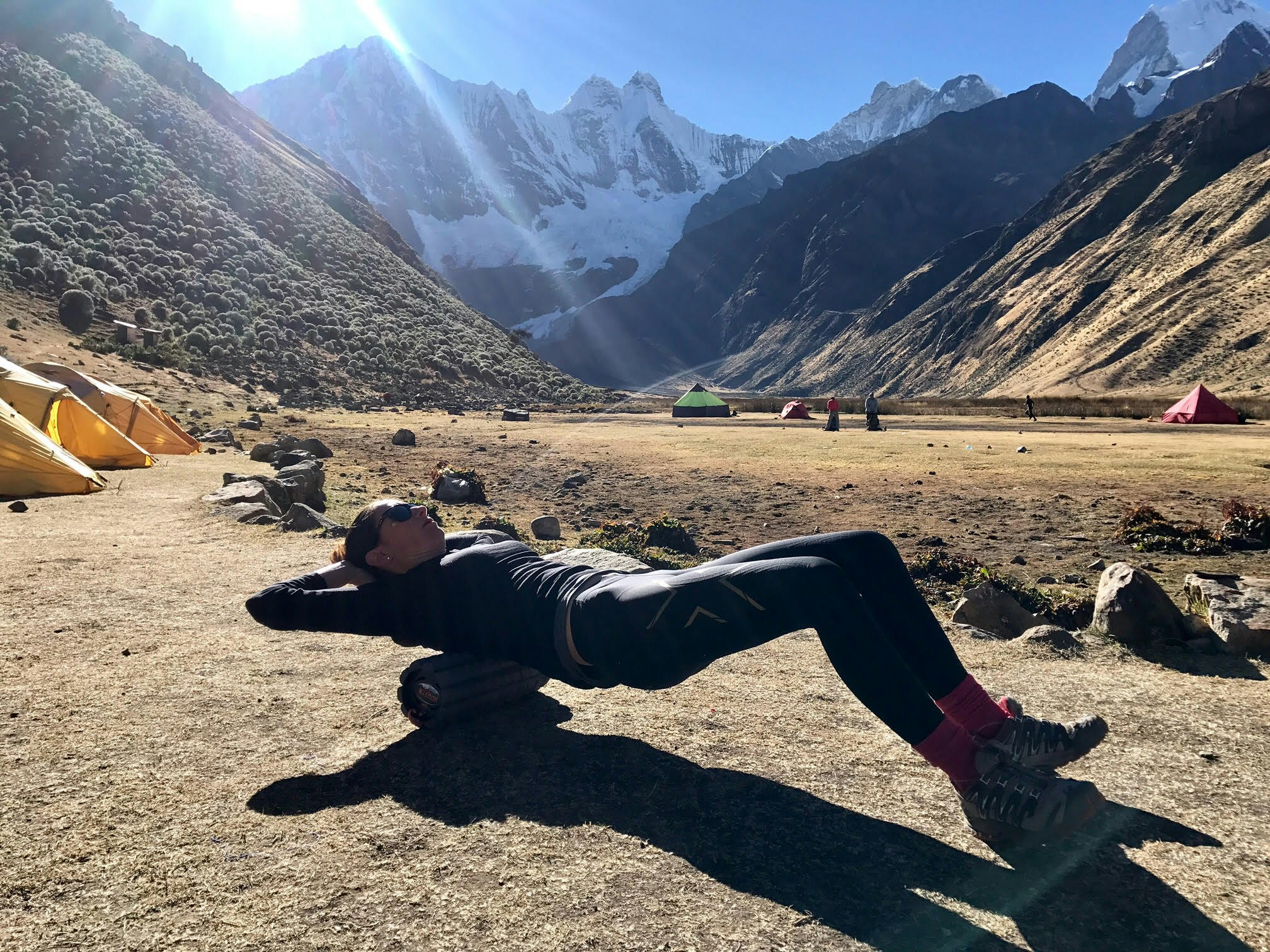 A woman lying on a Brazyn Morph collapsible foam roller at a campsite in the Andes mountains