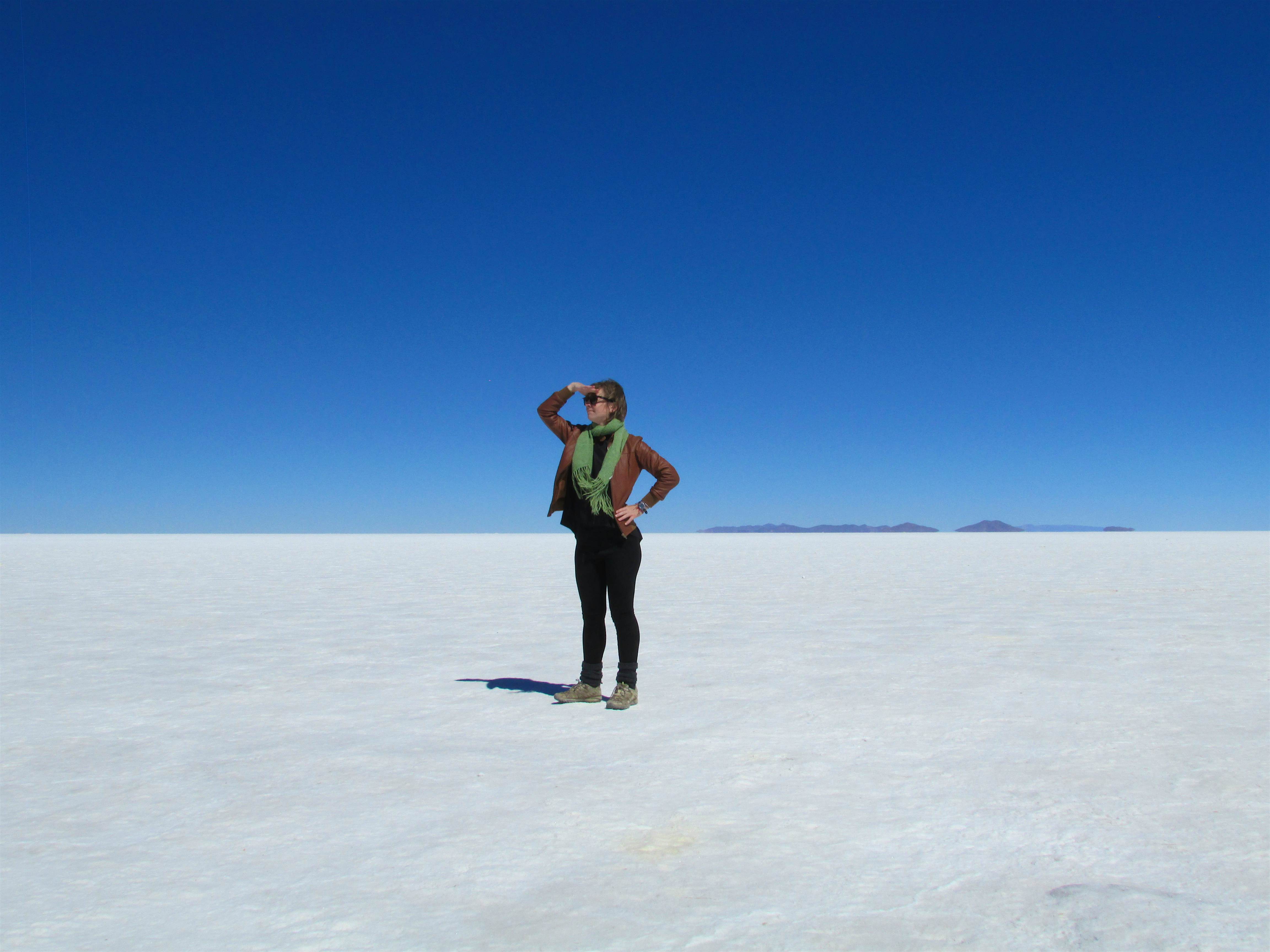 Britany in Bolivia (1).jpg A woman stands in the desert in Bolivia. The sand is bone white and the sky is a pale blue. She is posing by holding her right hand over her eyes.