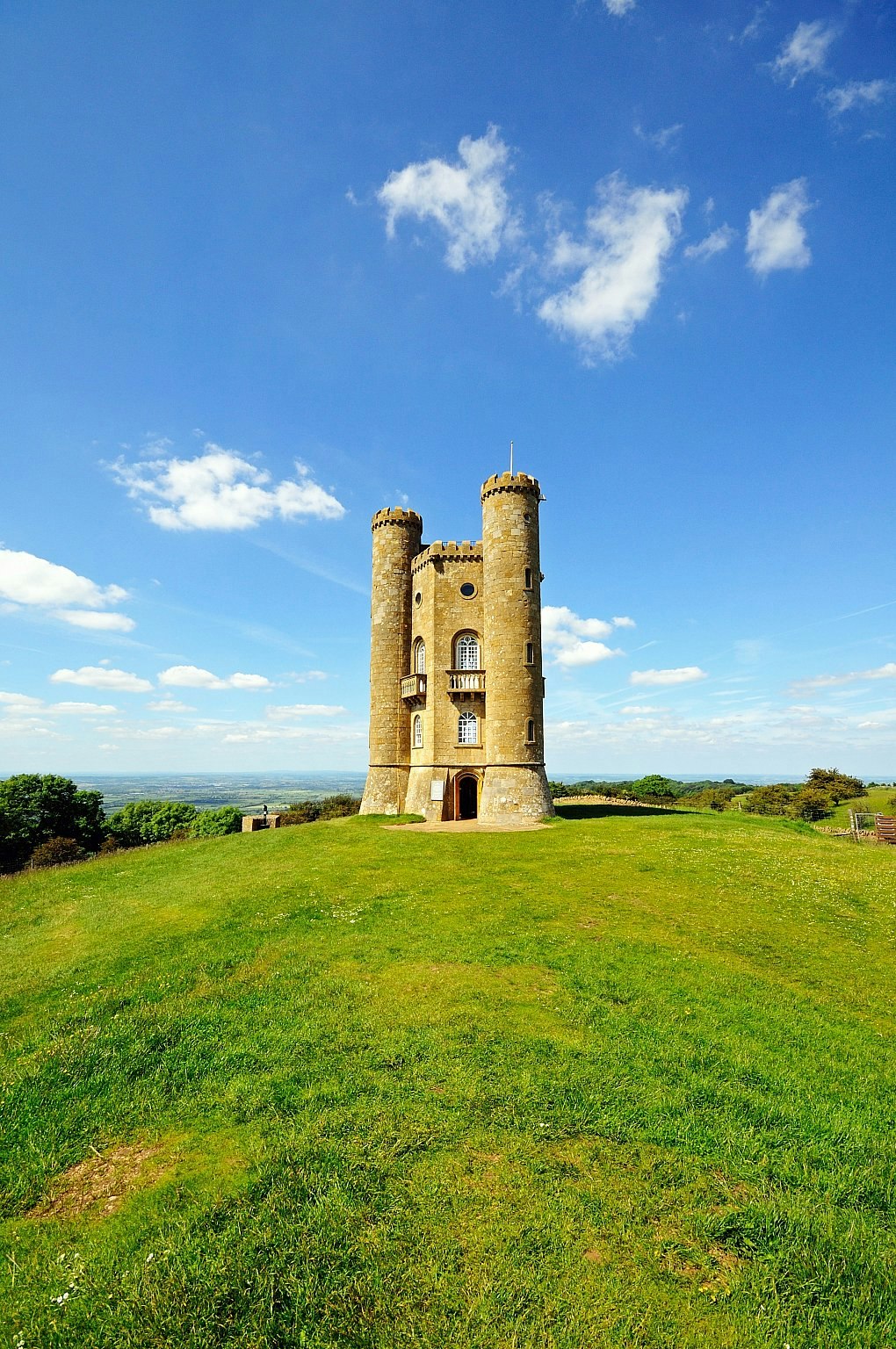 A turreted stone tower on a hilltop on a sunny day with panoramic views over the countryside beyond.
