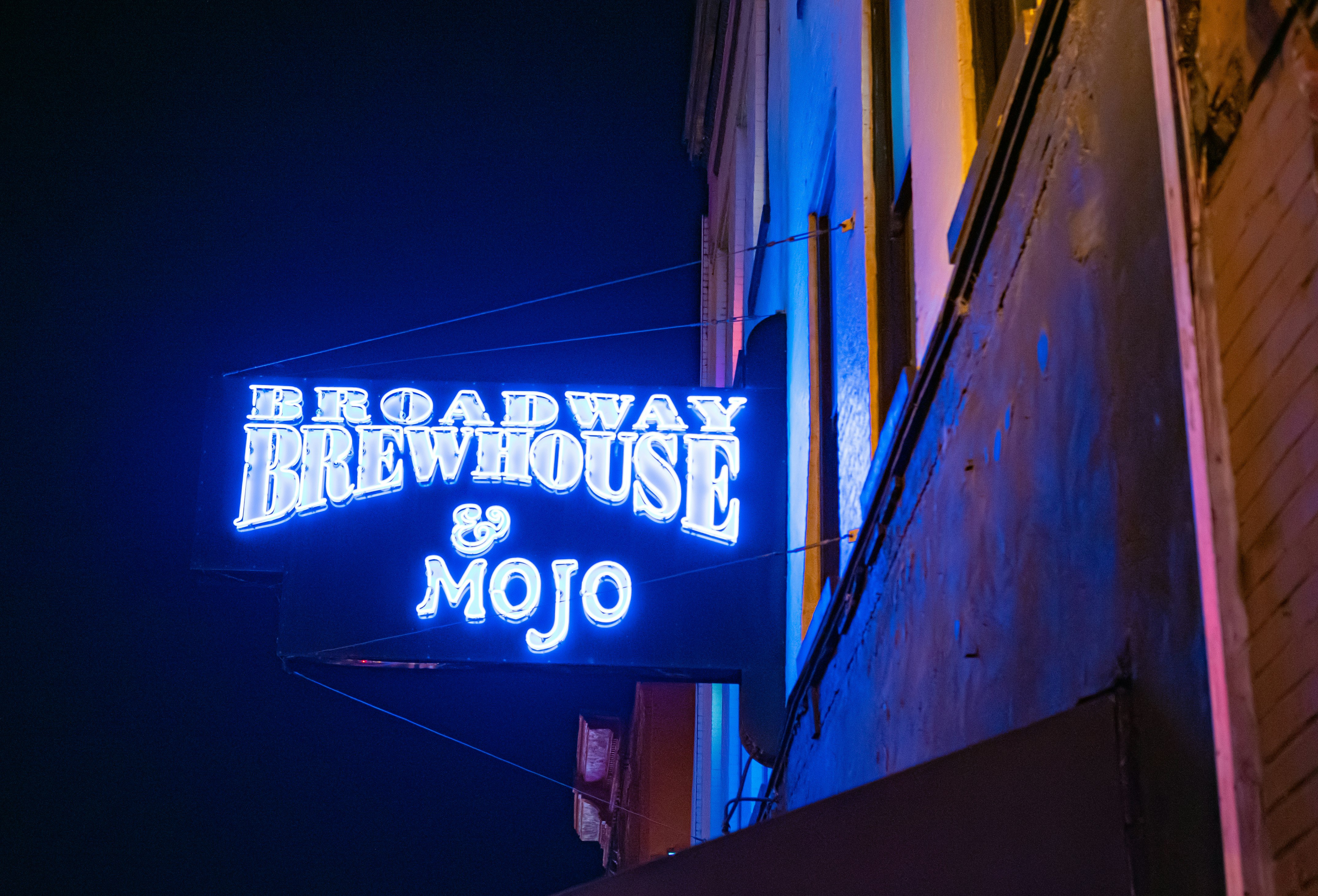 A neon sign hanging off the side of a building that says 'Broadway Brewhouse & Mojo'; NFL bars 
