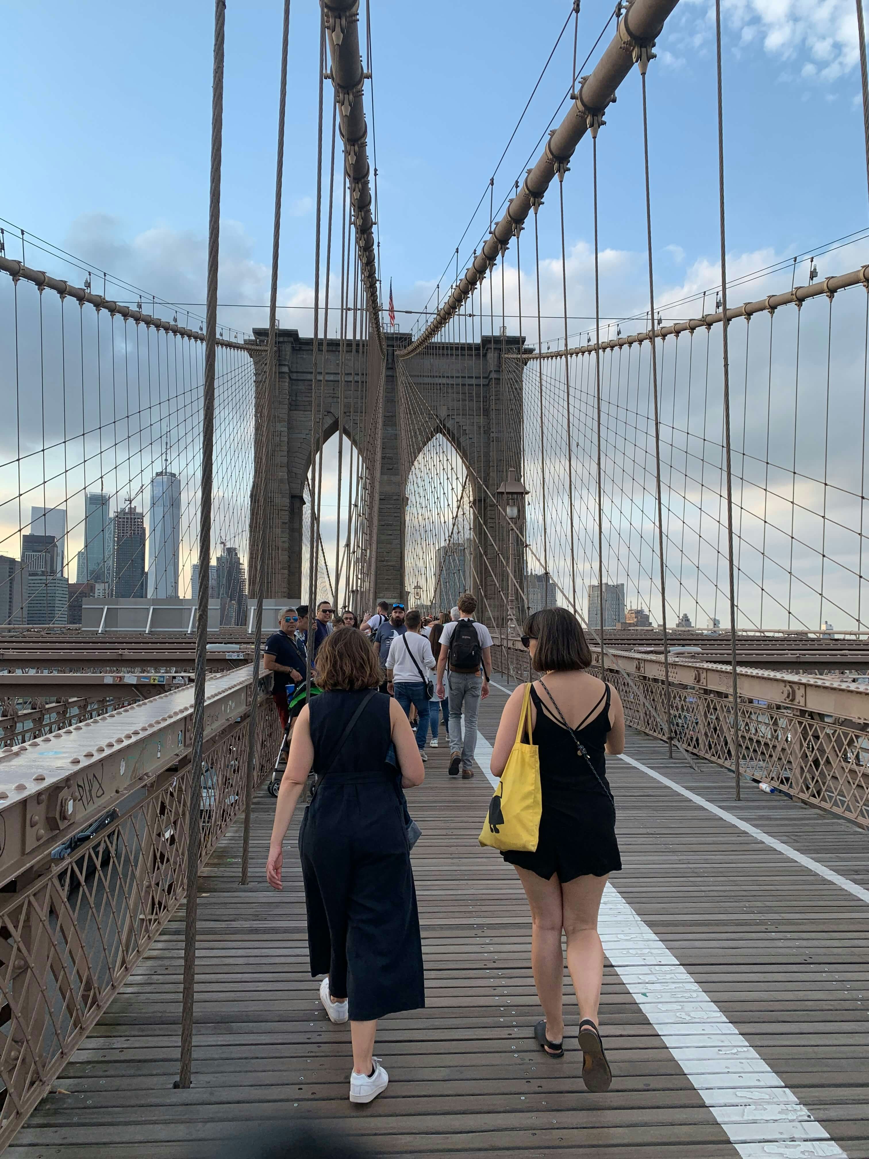 People walking across the Brooklyn Bridge. It is a clear, bright day.