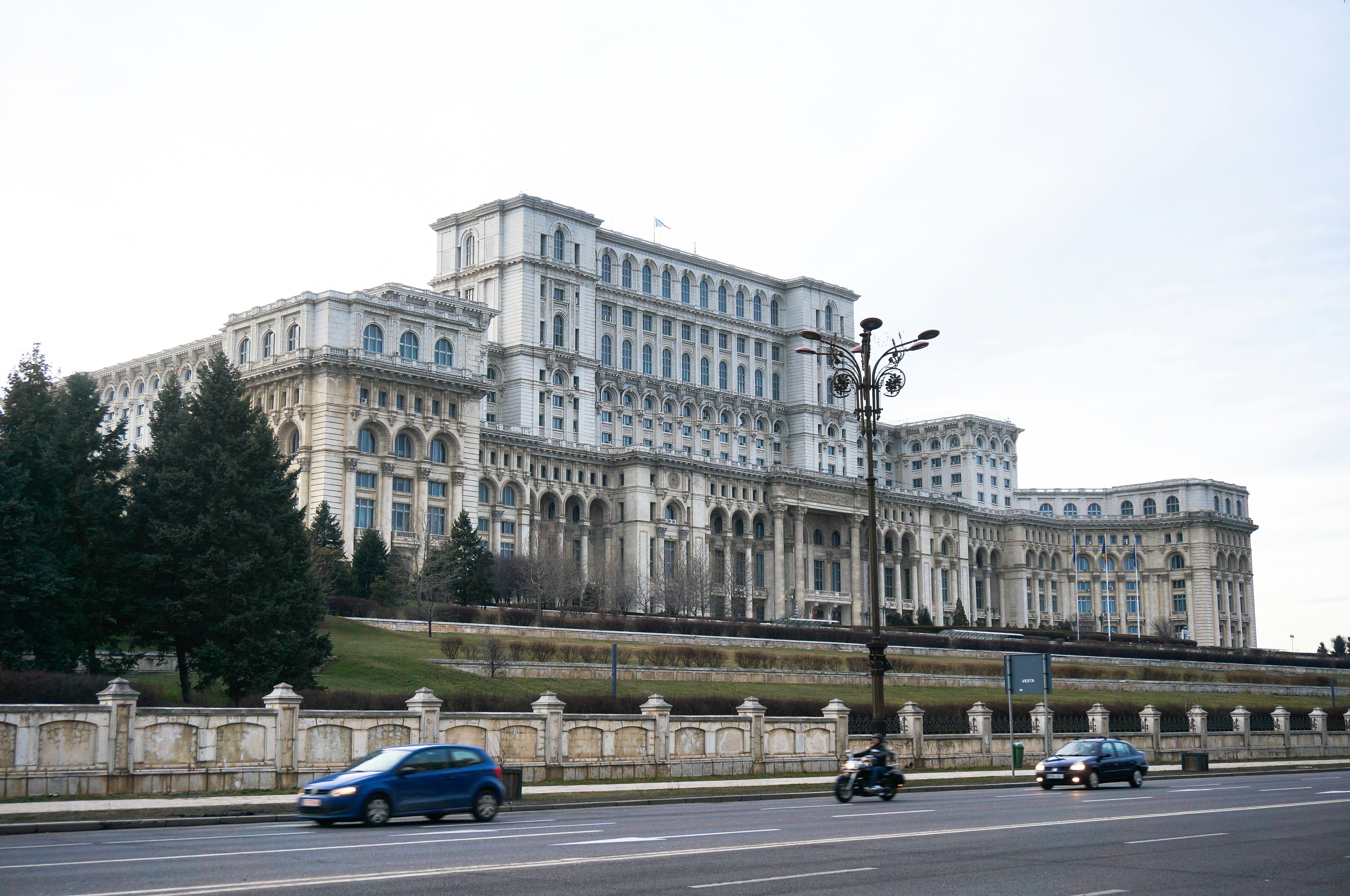 A side view of Bucharest's Palace of Parliament, a large tiered white stone building with hundreds of arched windows