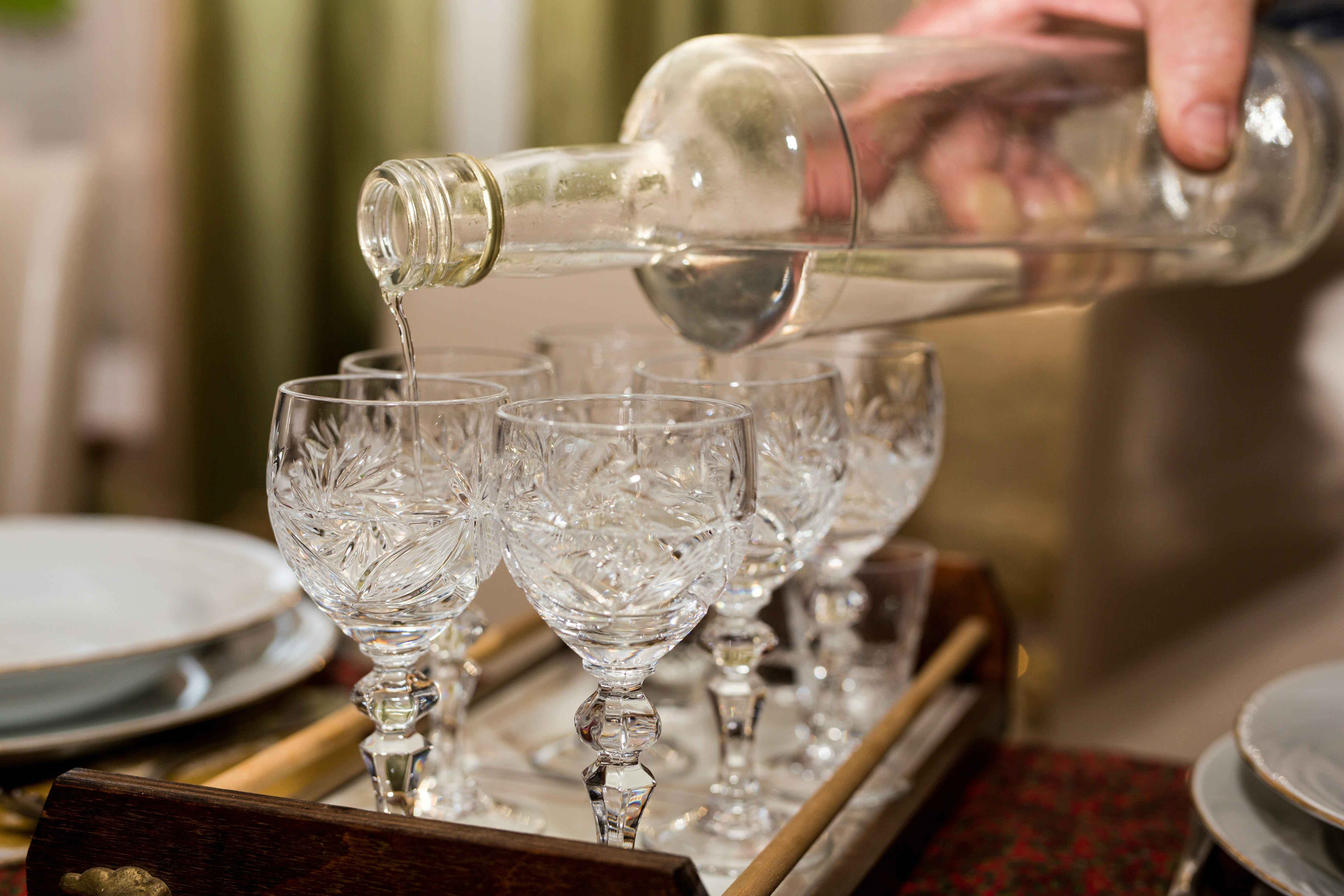 A hand pours clear Pálinka in a crystal glass on a tray of six crystal glasses; budapest autumn