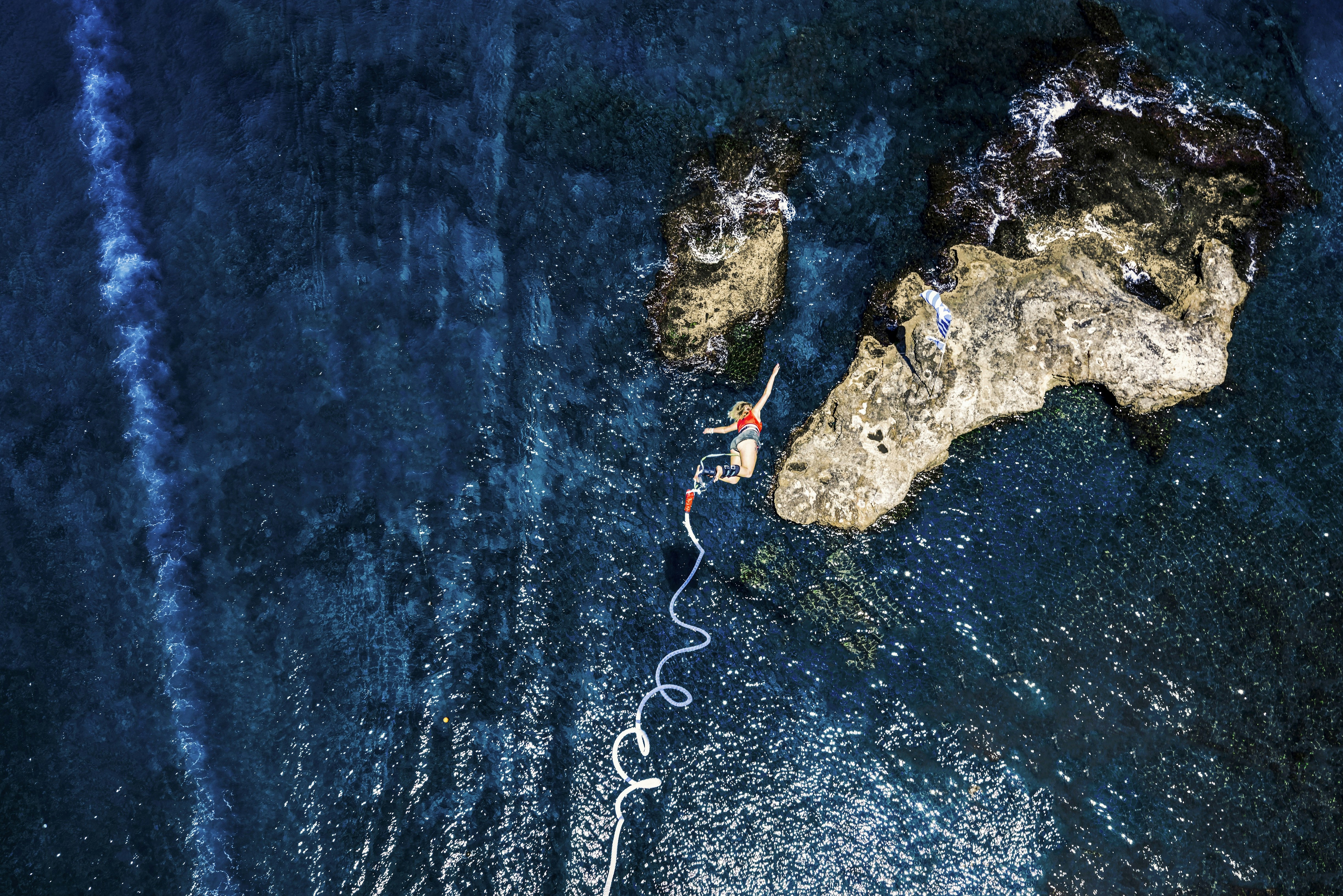 A top-down view of a woman bungee jumping above the blue sea in Greece.