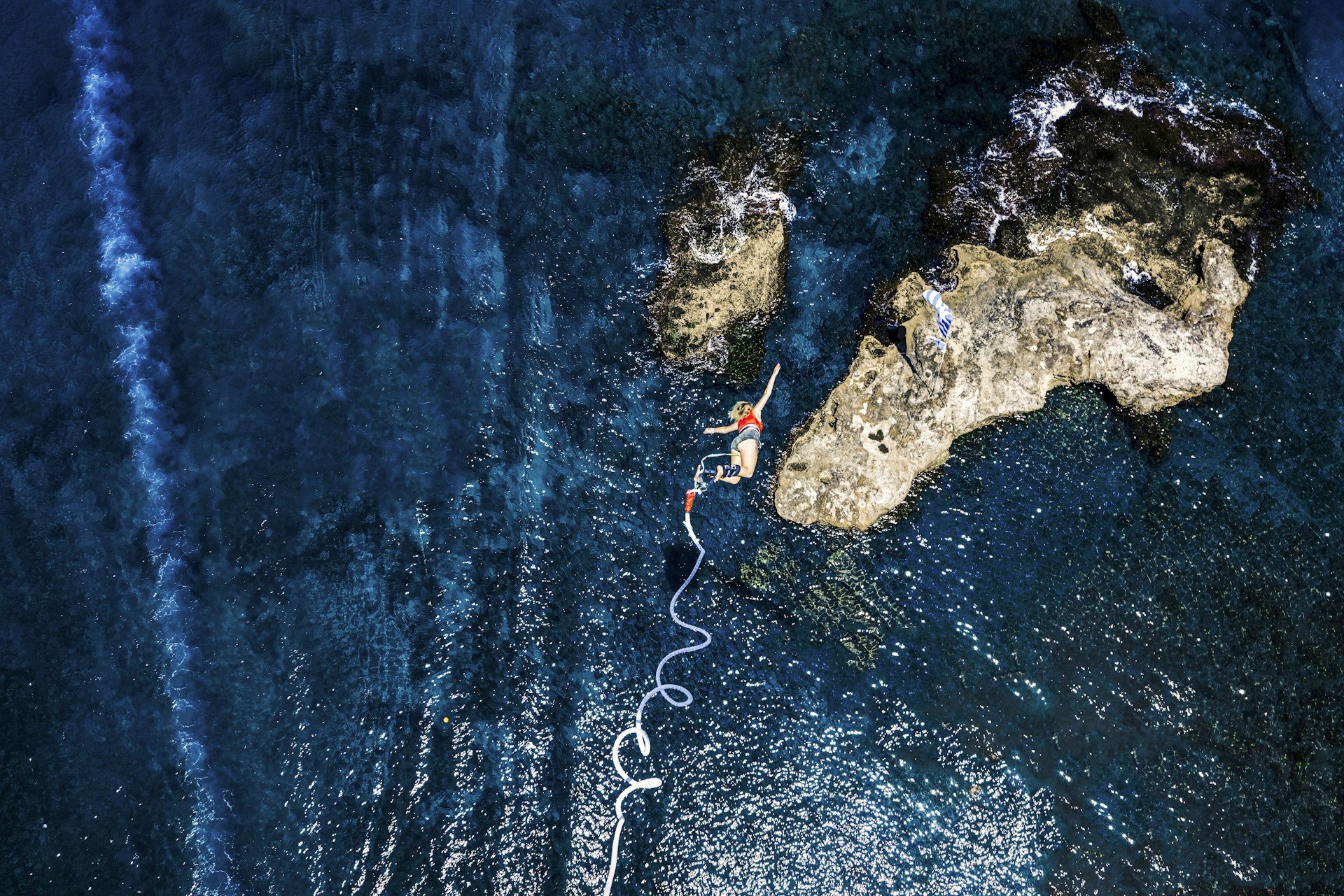 A top-down view of a woman bungee jumping above the blue sea in Greece.