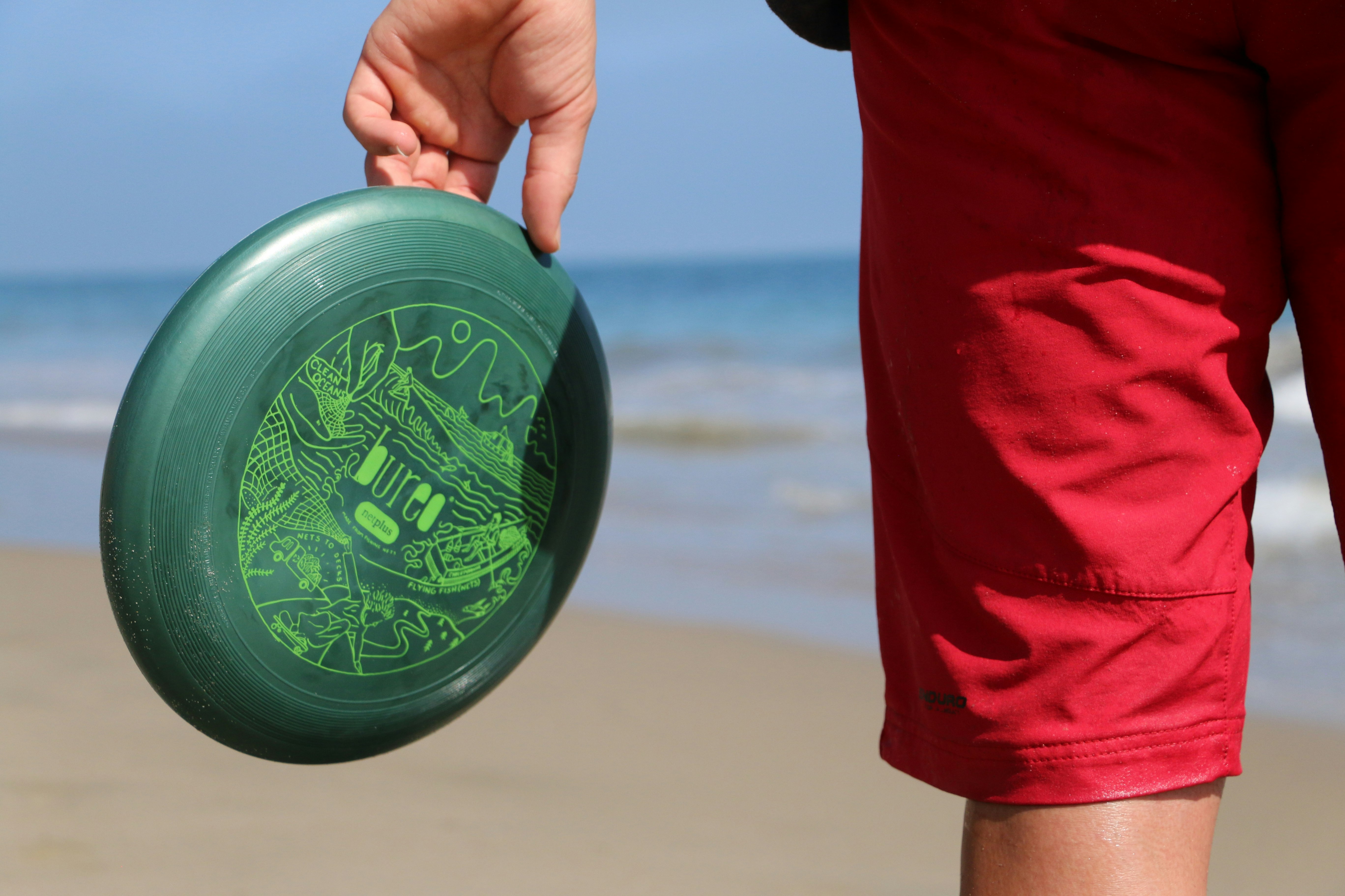 A closeup of a person in red shorts holding a Bureo frisbee