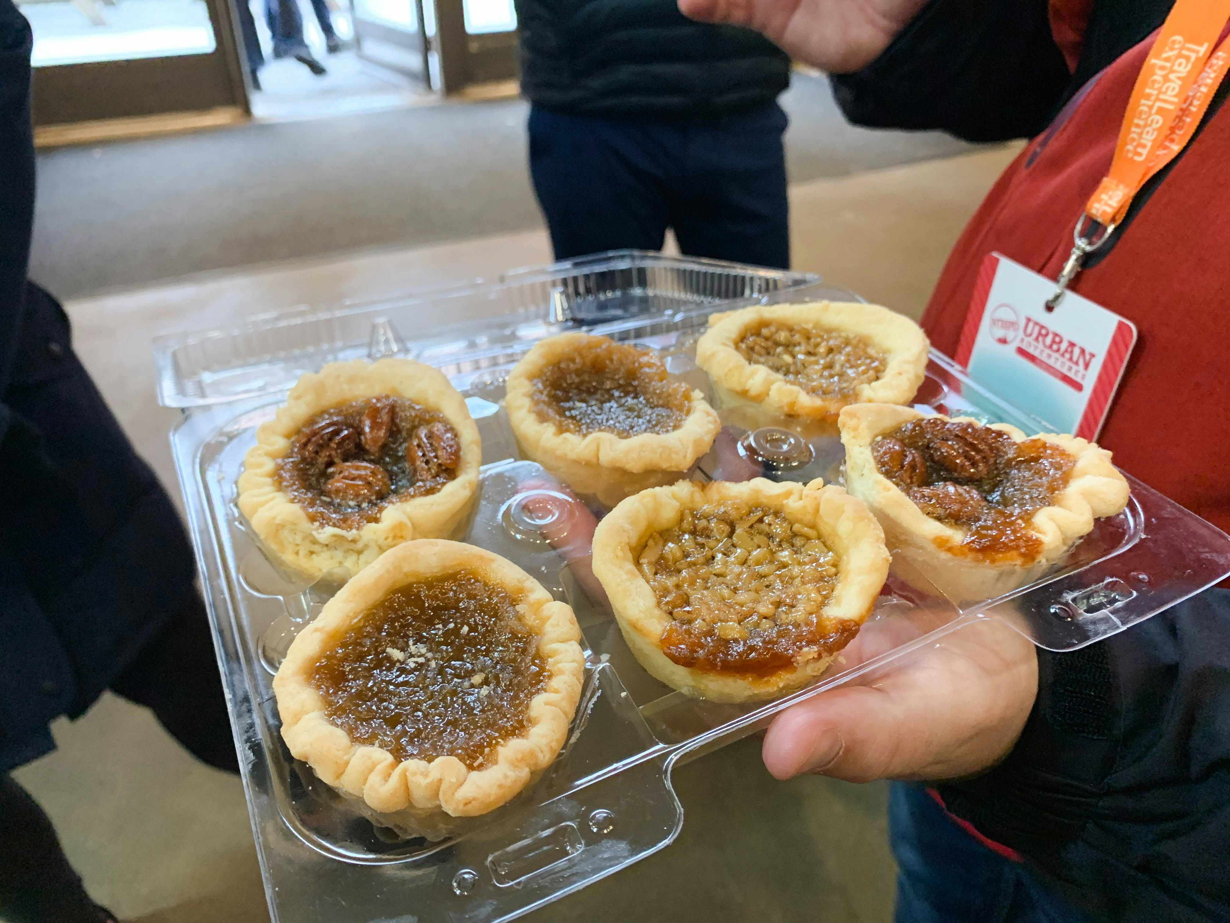 A hand holds a container with a selection of pastries in a plastic container. 