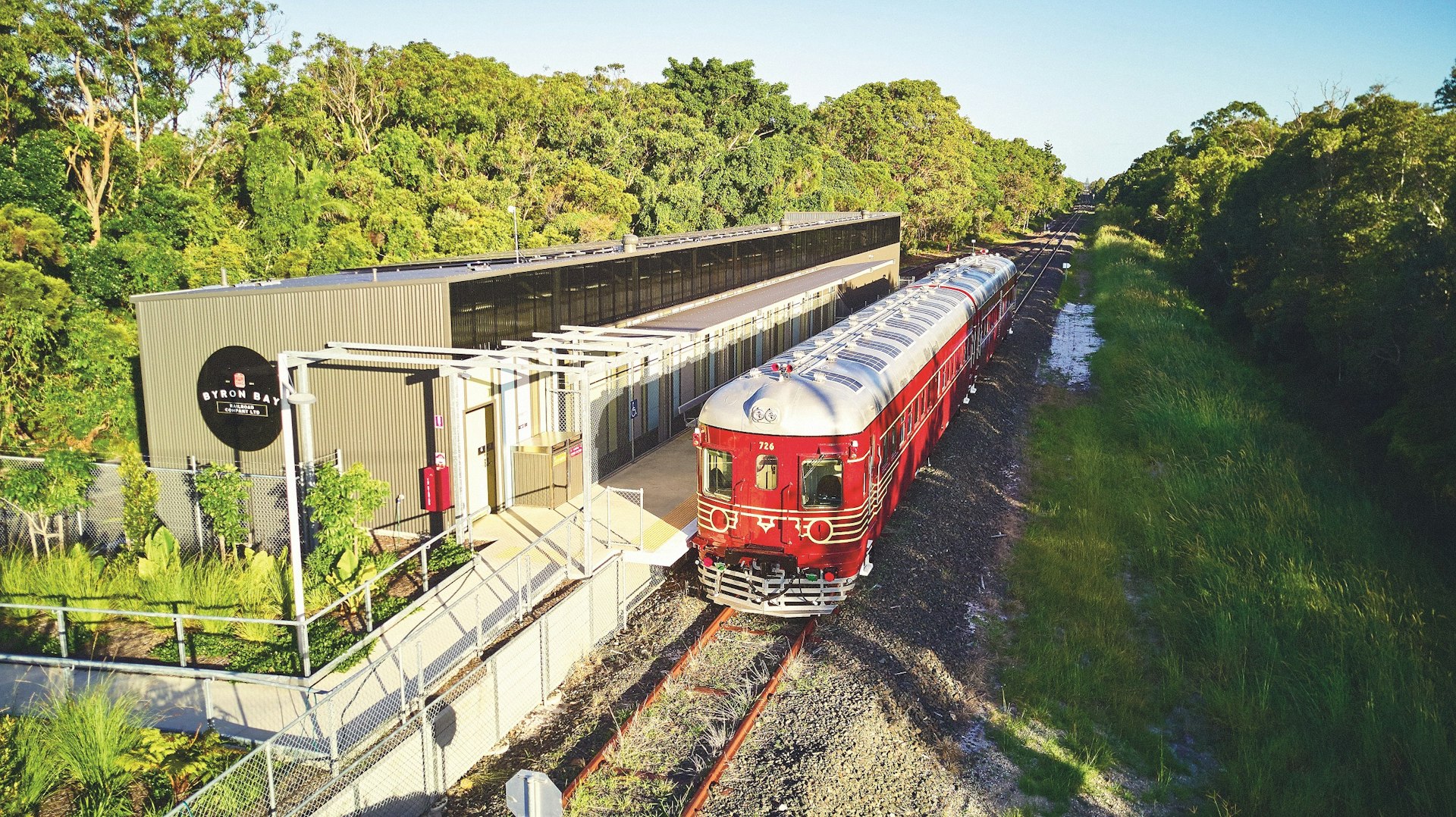 A red, two-carriage train stands outside a station. The roof of the train is covered in solar panels.