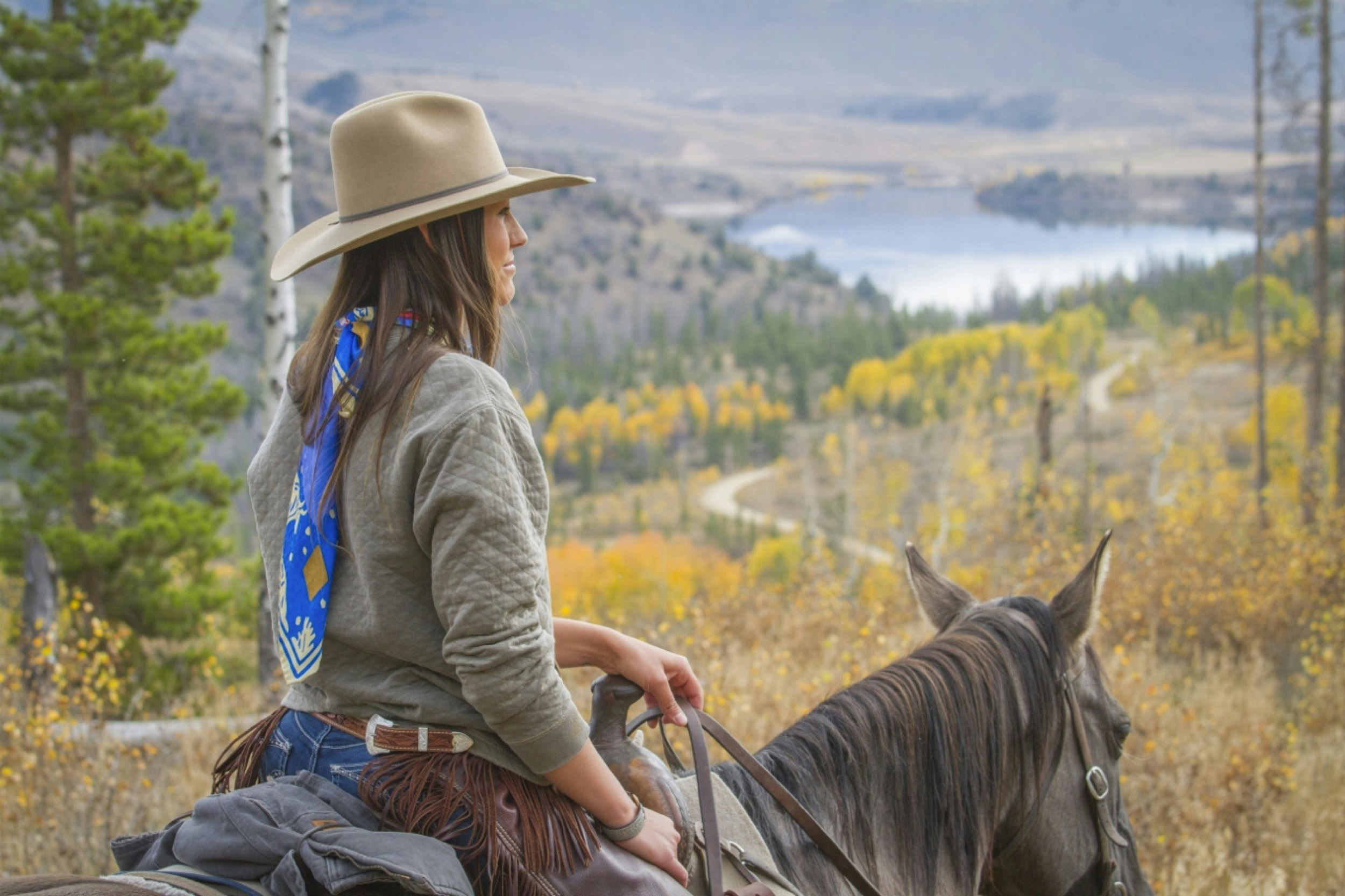 A woman rides a horse through the mountains of Colorado with a beautiful vista in the background; C Lazy U 100th birthday