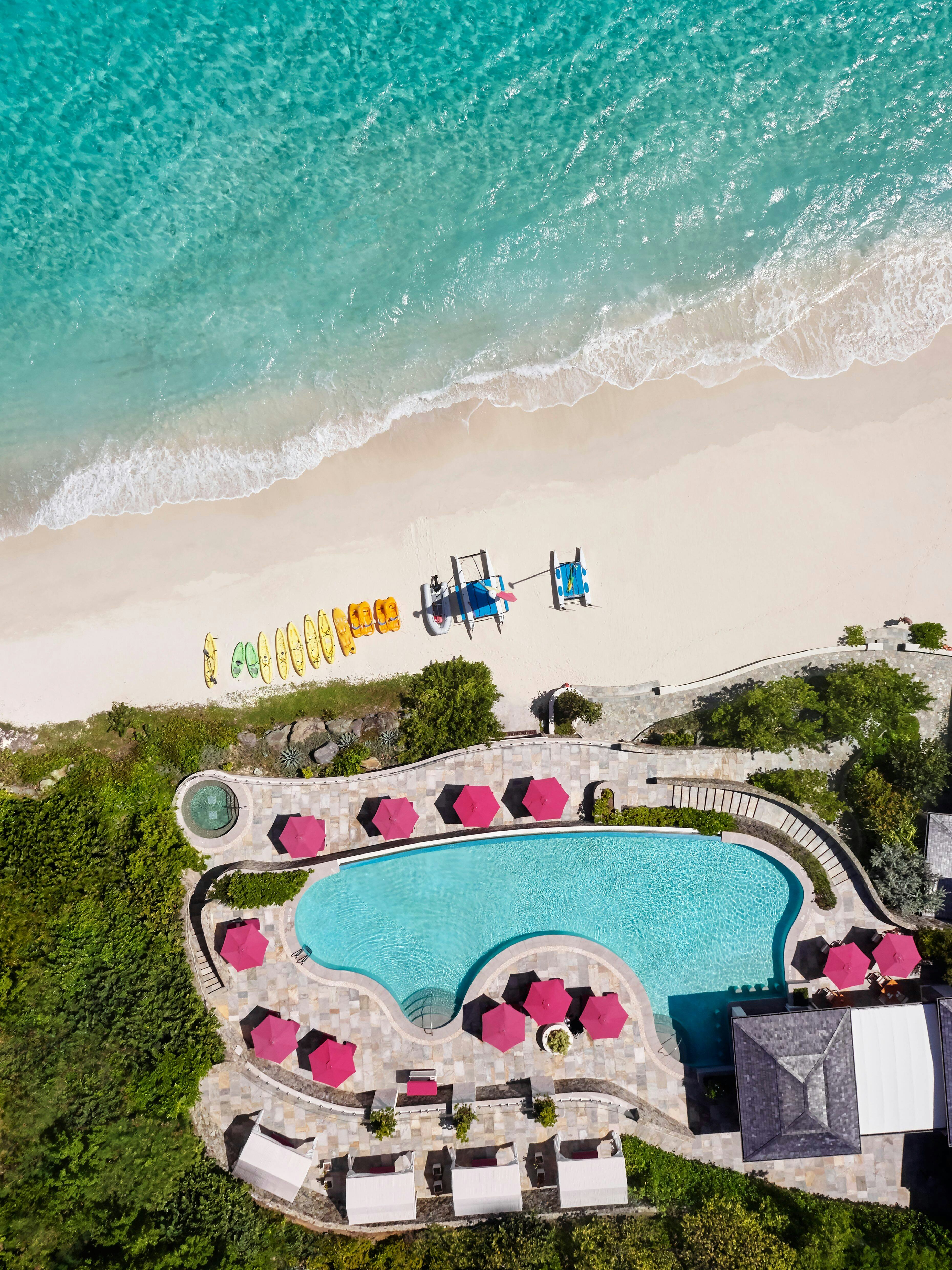 An aerial shot of the pool at the Mandarin Oriental, St Vincent and the Grenadines. Pink parasols are around the side of the pool. 