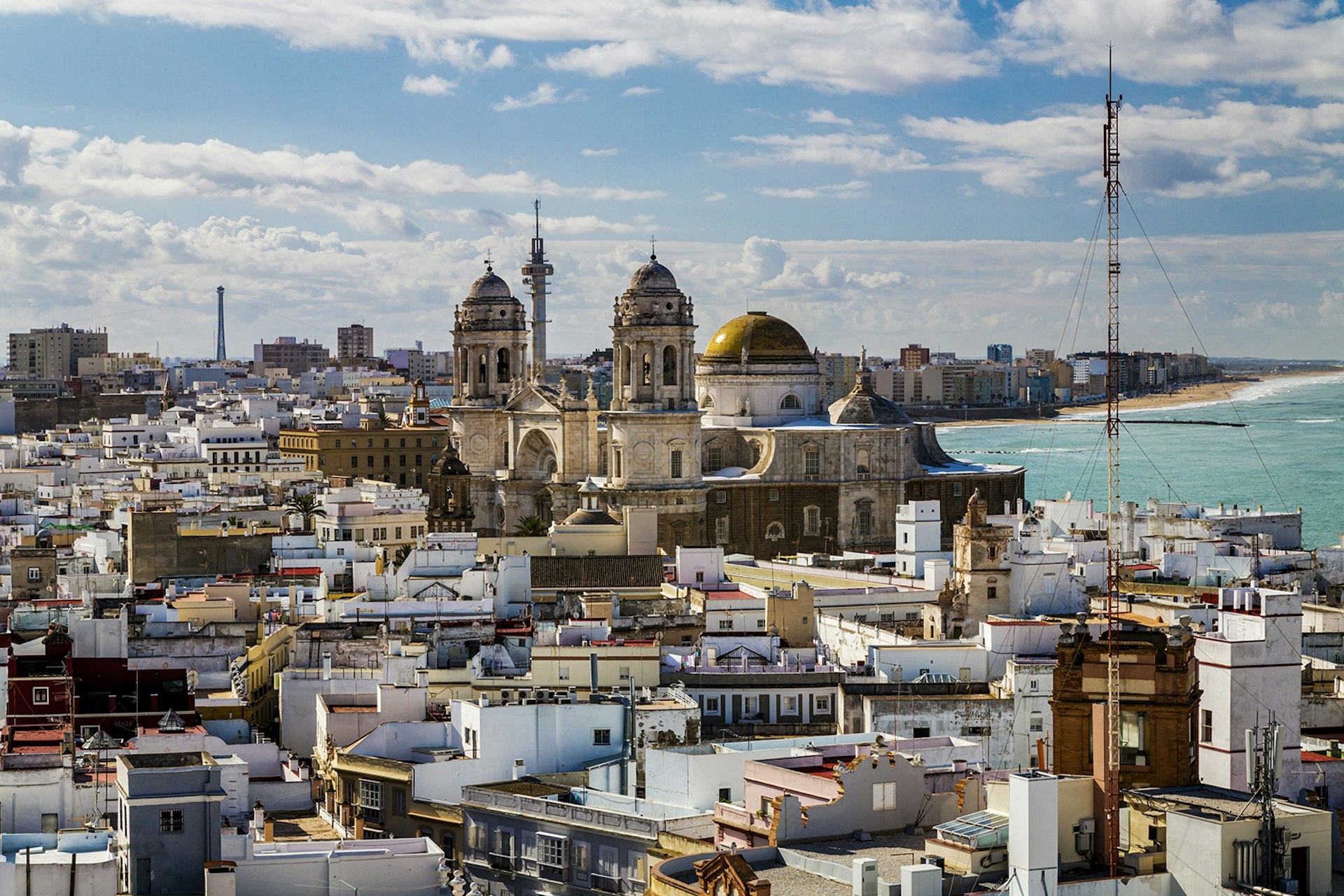 An aerial view of the city of Cádiz. The sea is visible, and the skyline is punctuated by a historic cathedral. Spain.
