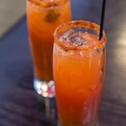 A pair of ruby colored Caesar drinks sit on a wooden bar 