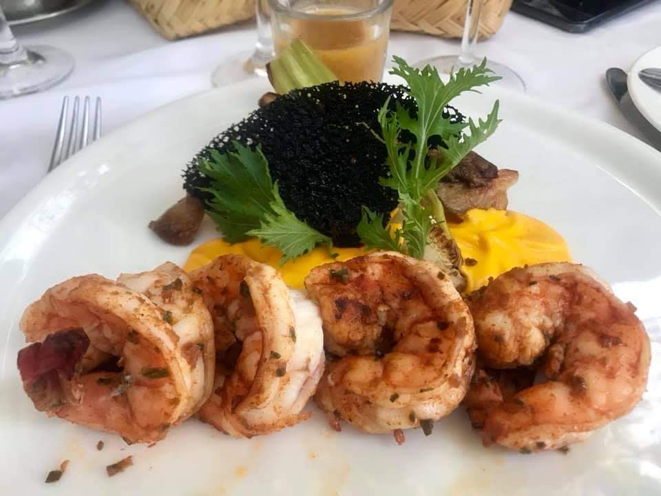 Four shrimp lay on a bed of bright yellow sauce which is topped with greenery and a black garnish