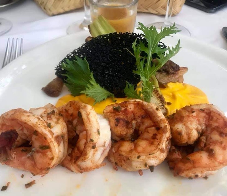 Four shrimp lay on a bed of bright yellow sauce which is topped with greenery and a black garnish