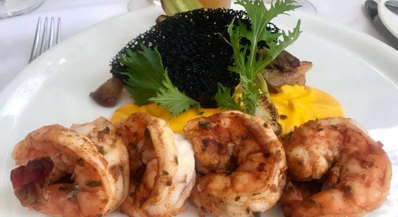 Four shrimp lay on a bed of bright yellow sauce which is topped with greenery and a black garnish