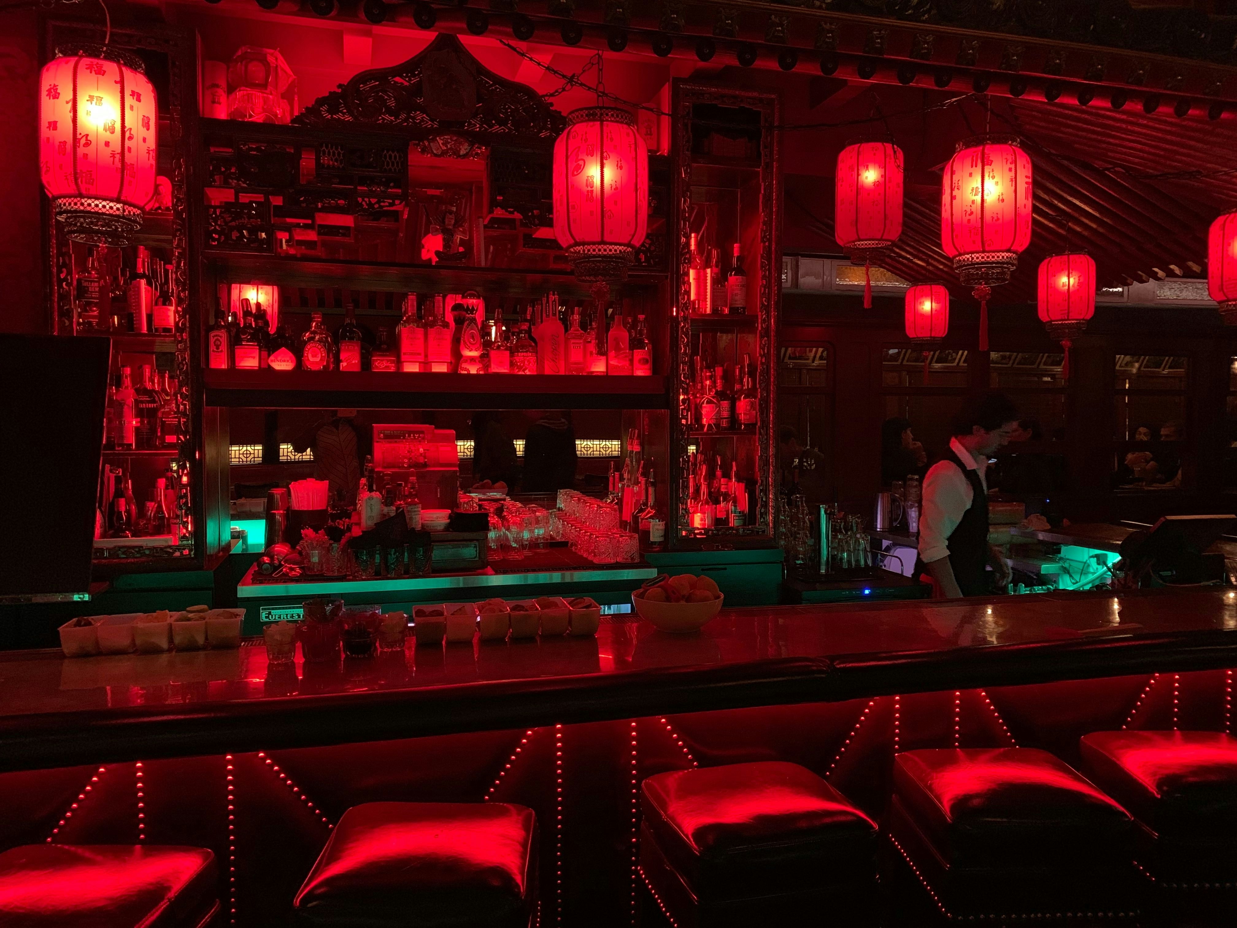 Red paper lanterns hang from the bar ceiling at The Cafe Formosa, casting a red light over the entire area. There is a bartender working on the side.