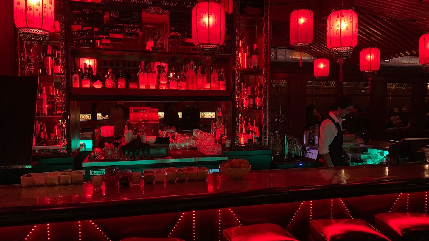 Red paper lanterns hang from the bar ceiling at The Cafe Formosa, casting a red light over the entire area. There is a bartender working on the side.
