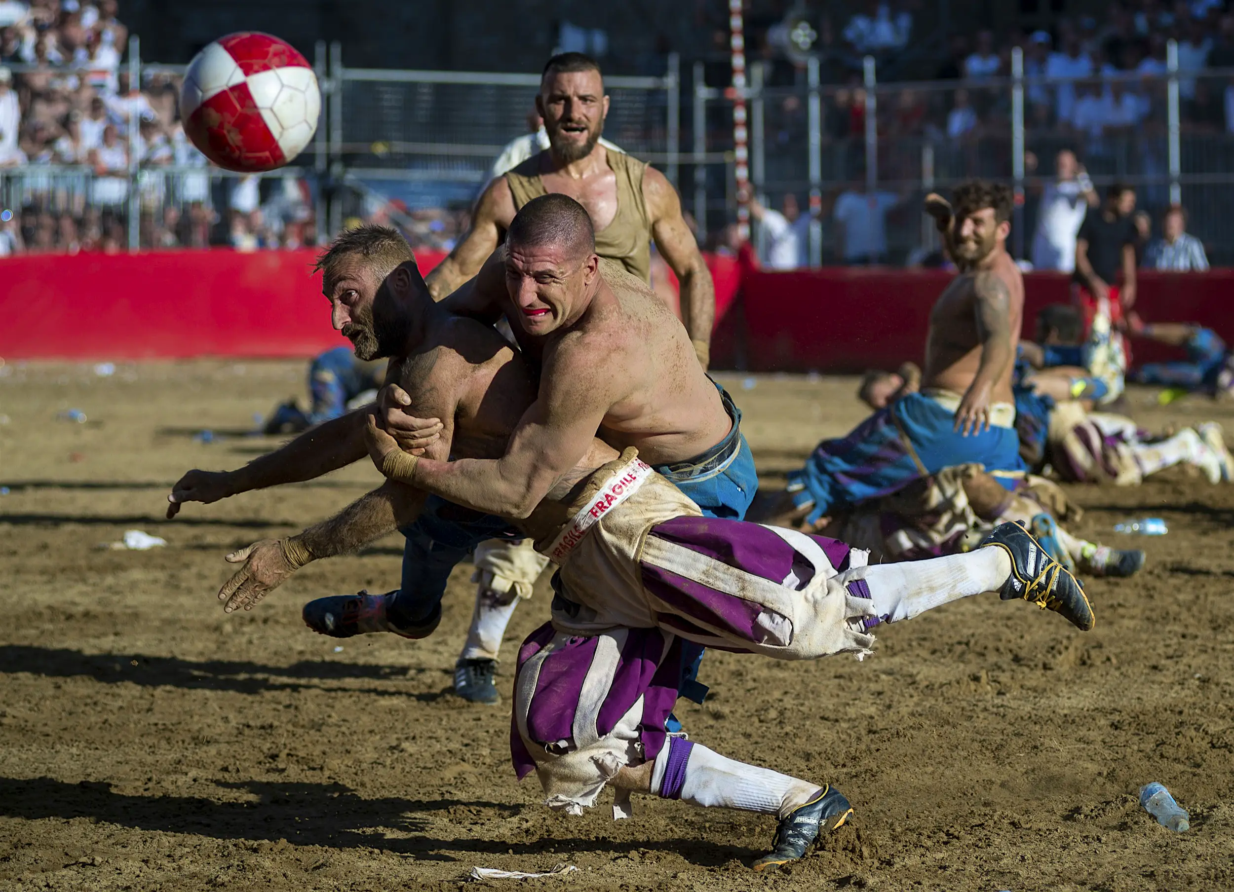 Calcio_Storico.jpg A man is tackled in a muddy arena as both men - and others around them - watch a ball bouncing erratically; unique sporting events