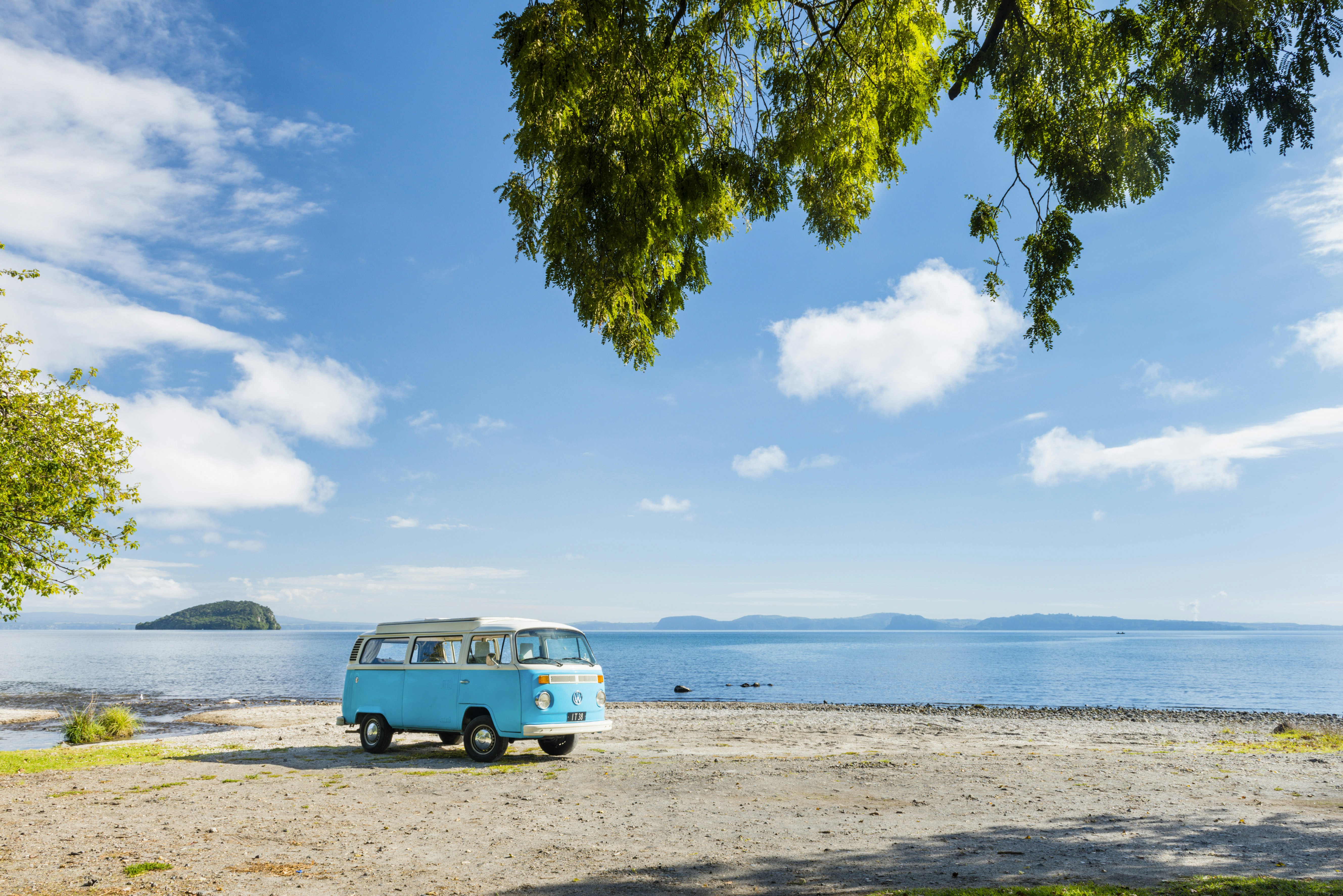 A blue VW camper van parked on a sandy beach with a lake in the background