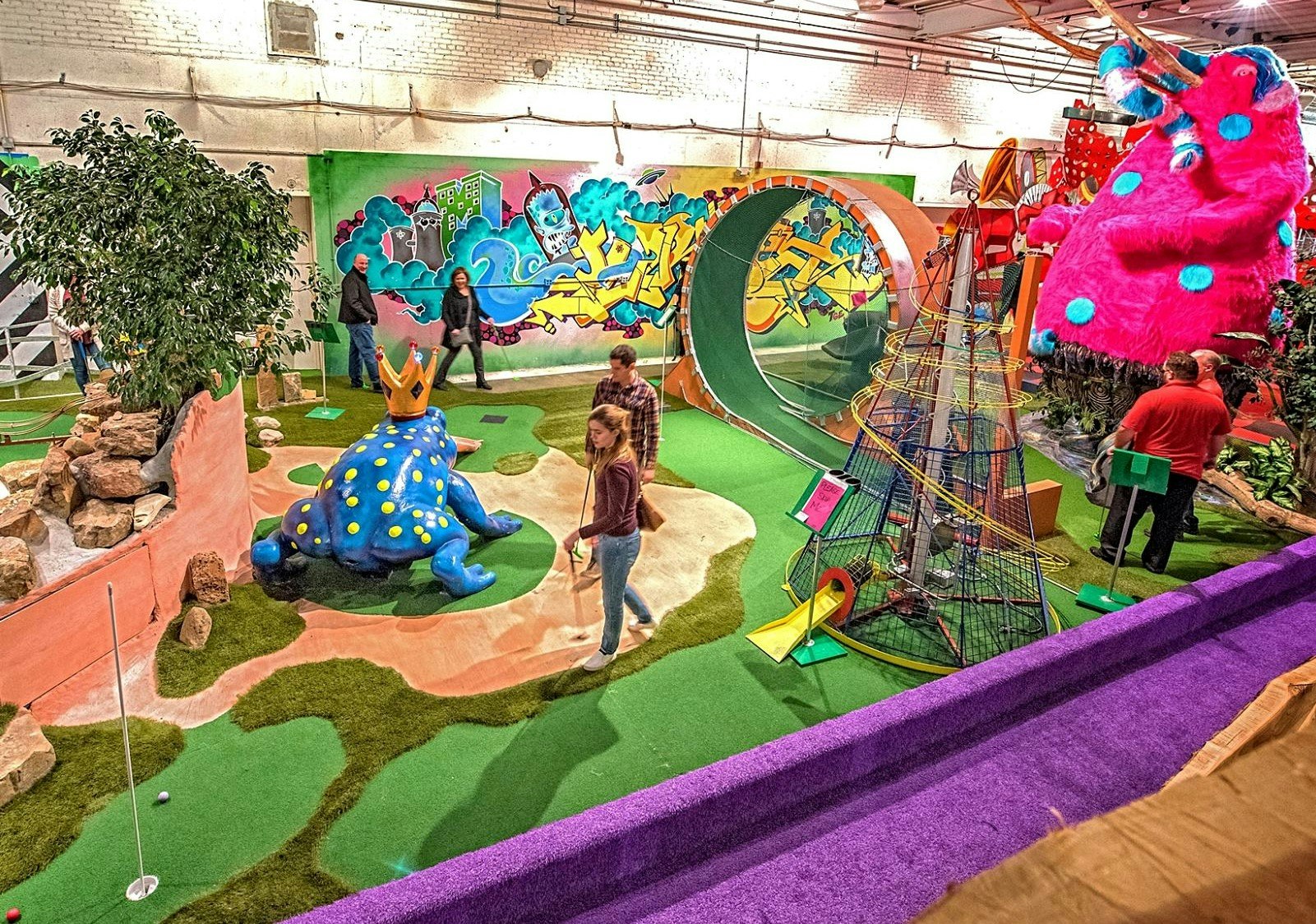 An aerial view of the mini golf course at Can Can Wonderland, which contains novelty objects like a giant frog and large 'loop the loop' structure.