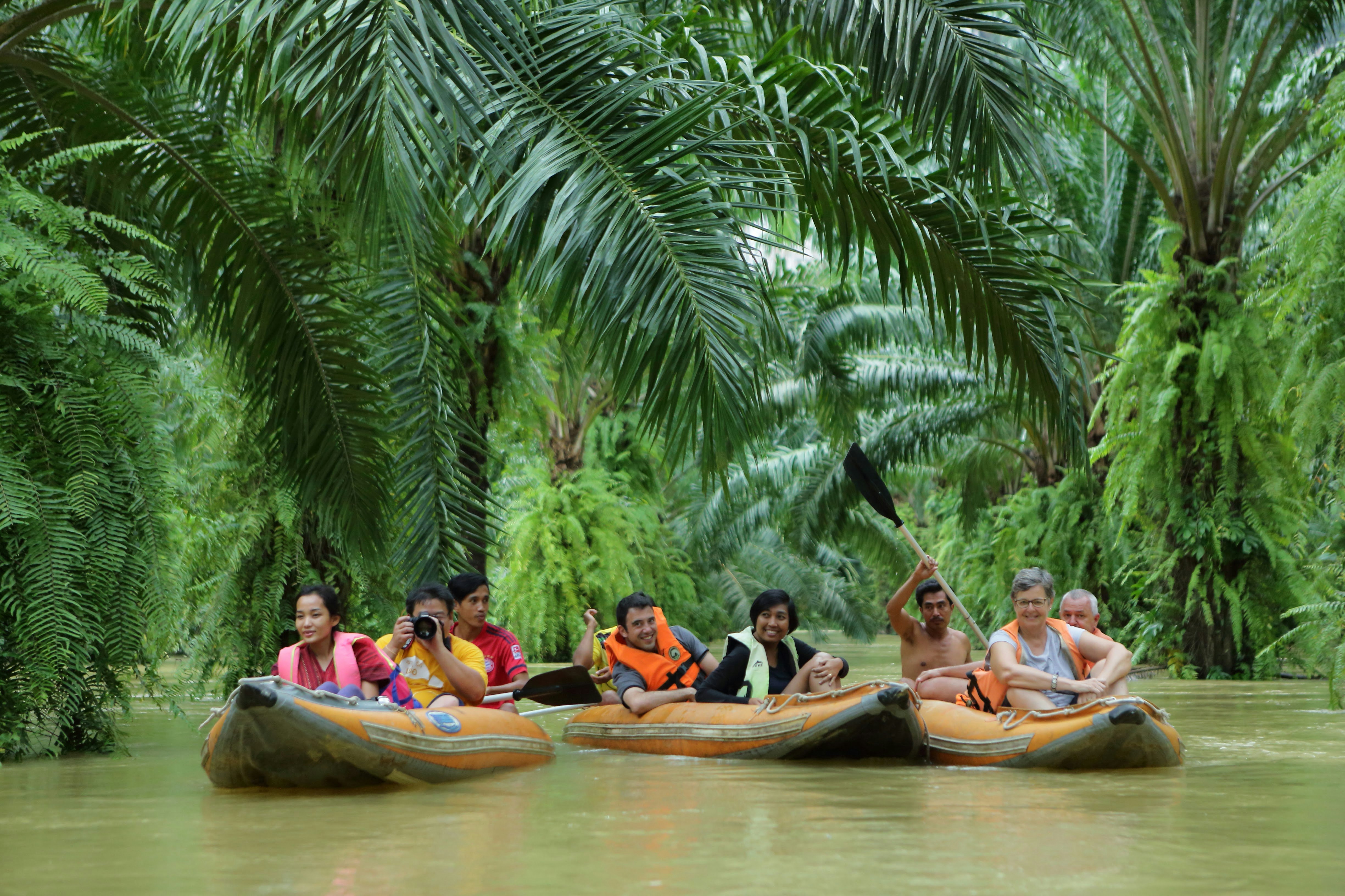 Three canoes each carrying three people sit low in the murky water in river flowing through a dense jungle