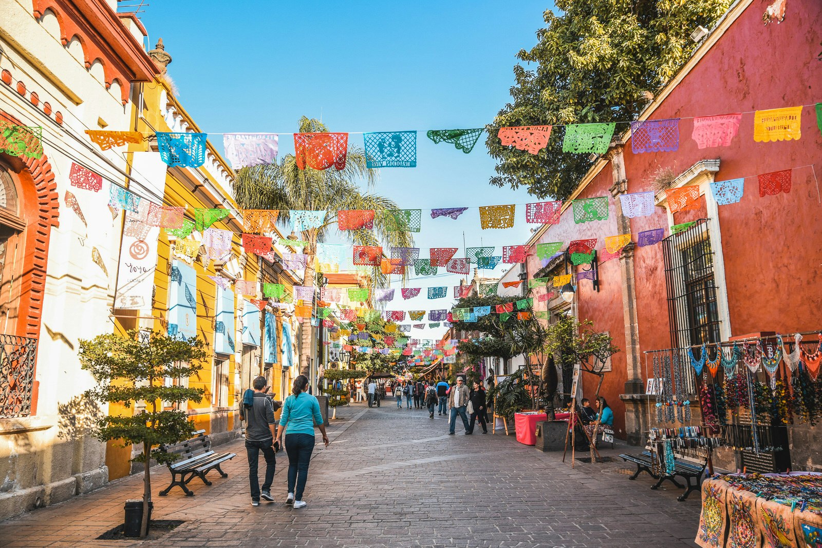 En gata i Tlaquepaque, Guadalajara, Mexiko på en solig dag.  Den kullerstensbelagda gatan pryds av färgglada fyrkantiga bunting. 