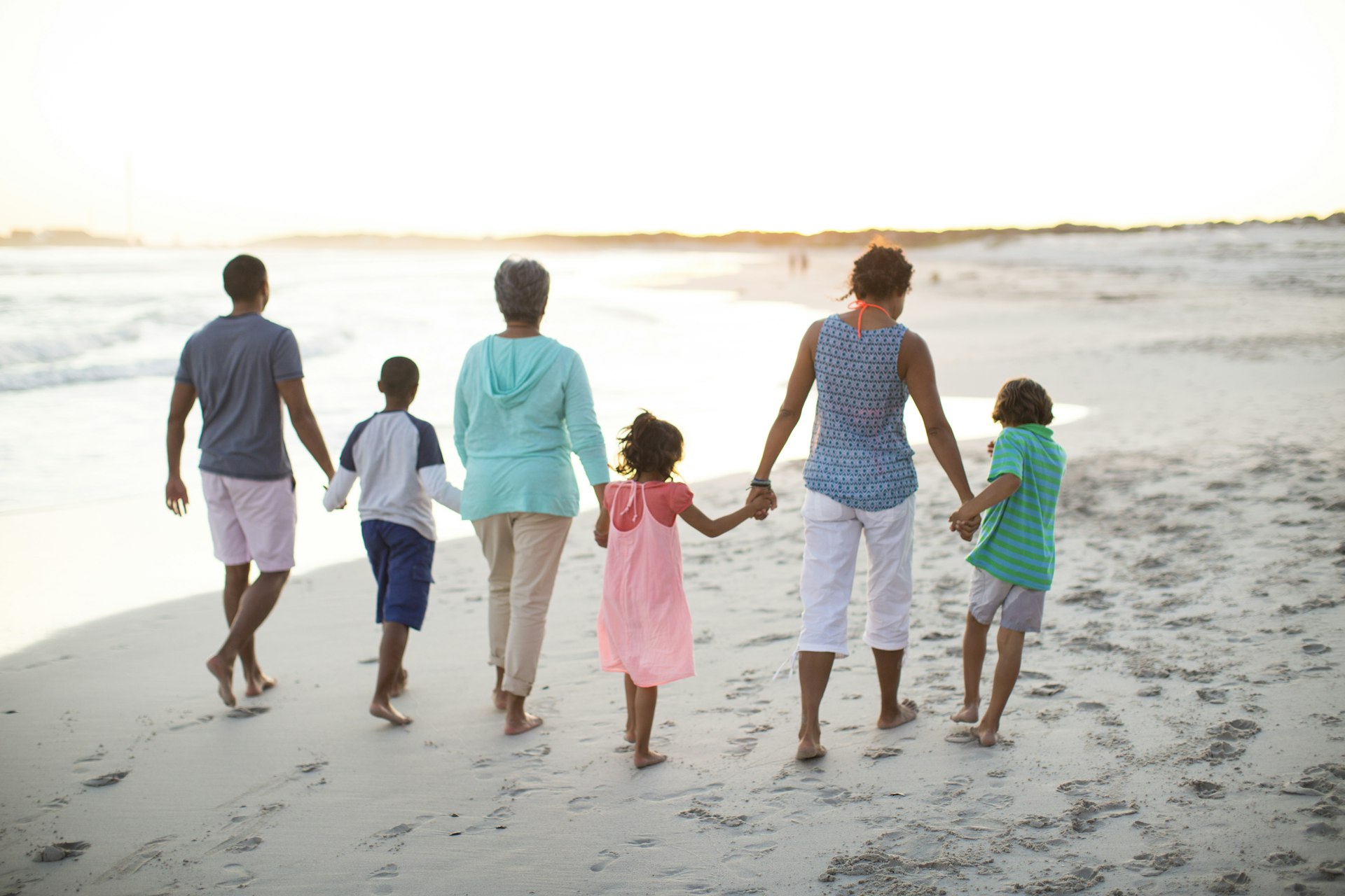 Family, with children, parents and grandmother, walking together along the beach at sunset.