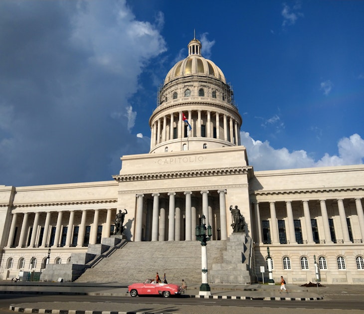 A hot pink classic car is parked in front of the newly renovated Capitolio Nacional