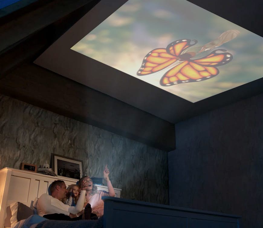 En familj tittar förundrat i taket när en fjäril projiceras ovanför dem