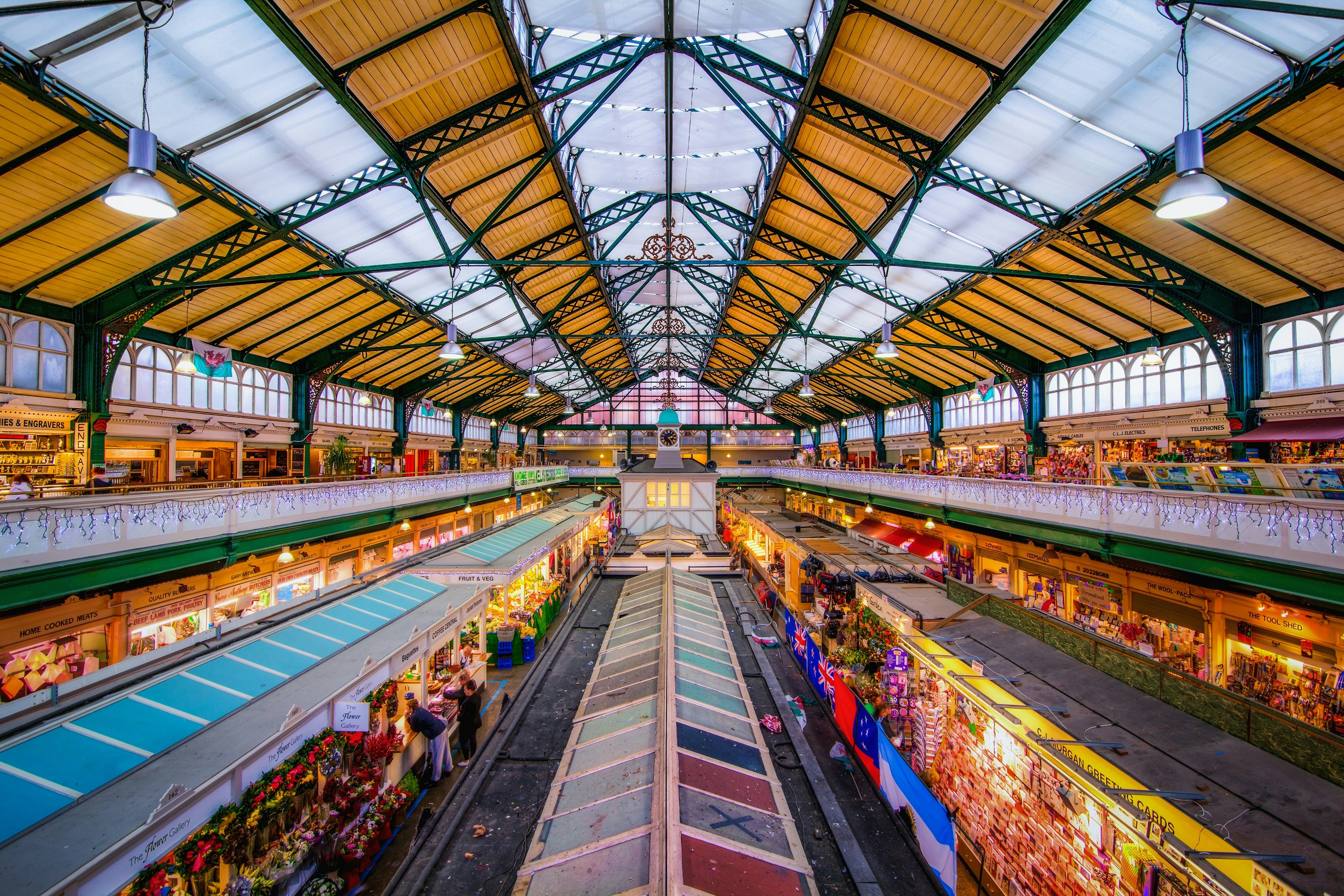 An aerial view of the interior of the indoor market in Cardiff, with two lines of stalls running down the centre of the building. Small shops and businesses also line the balcony on the building's second floor.