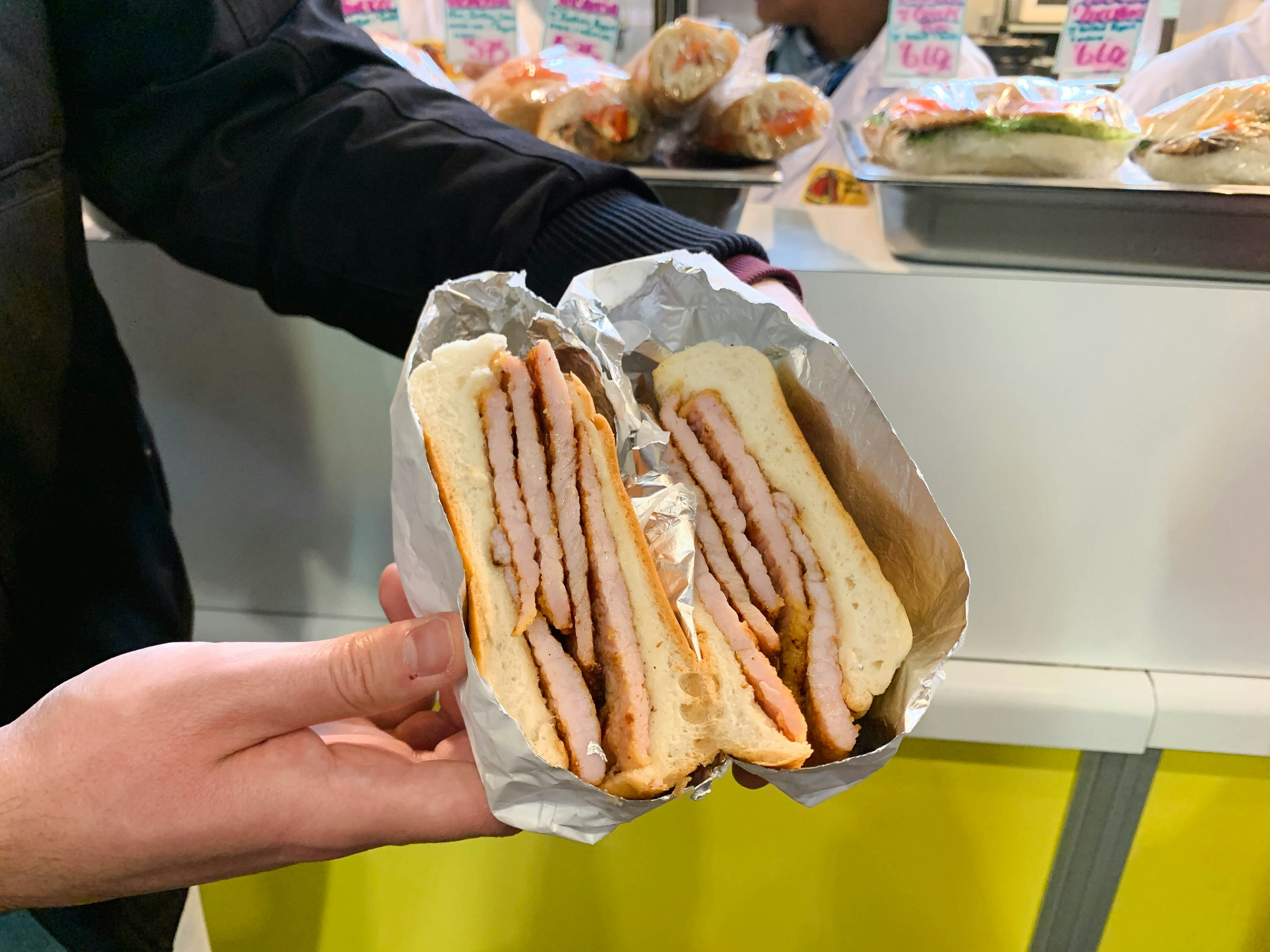 A hand holding a sandwich filled with thick slices of Canadian bacon