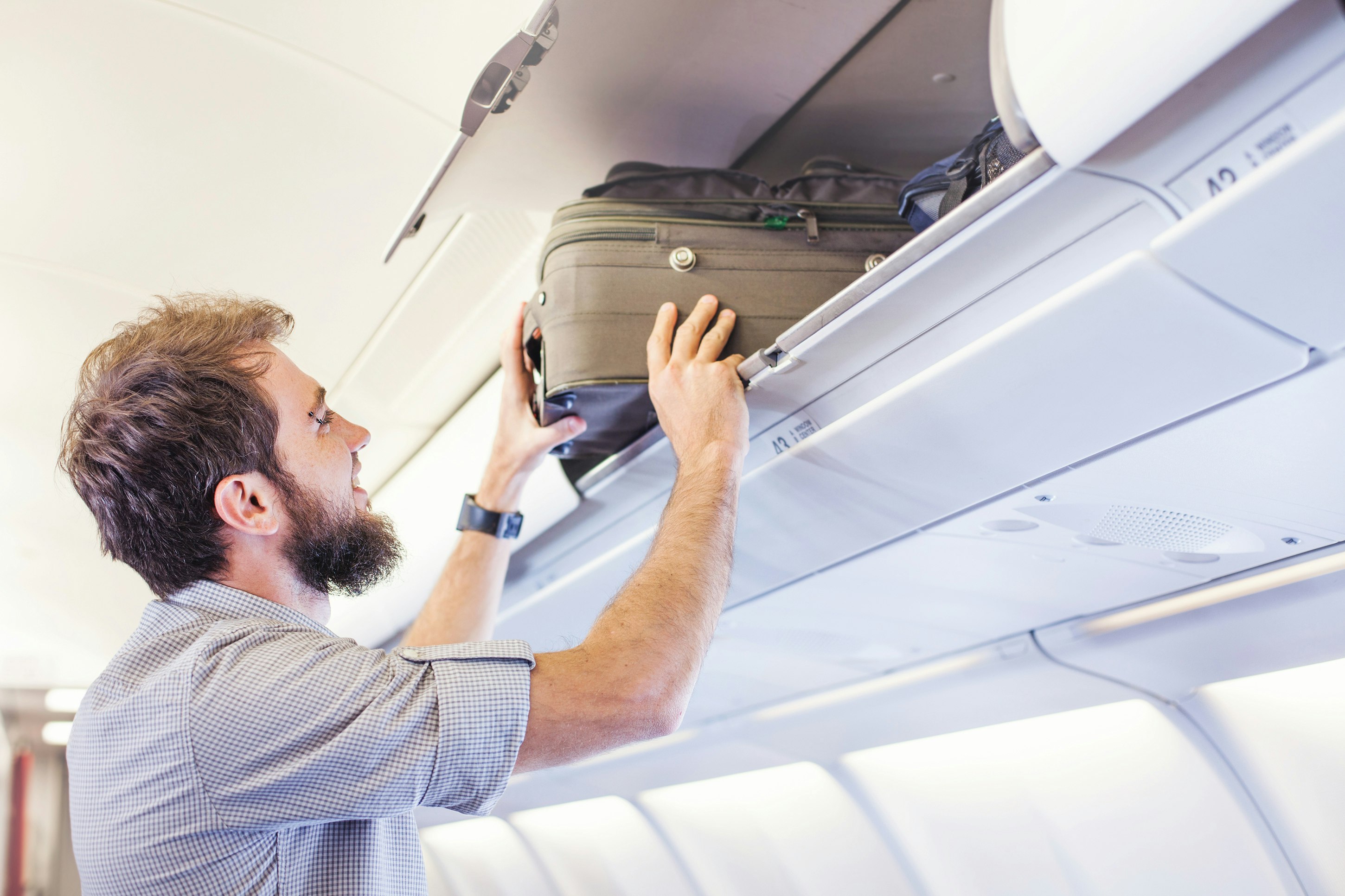 A passenger on a plane is placing his carry-on luggage in an overhead compartment.