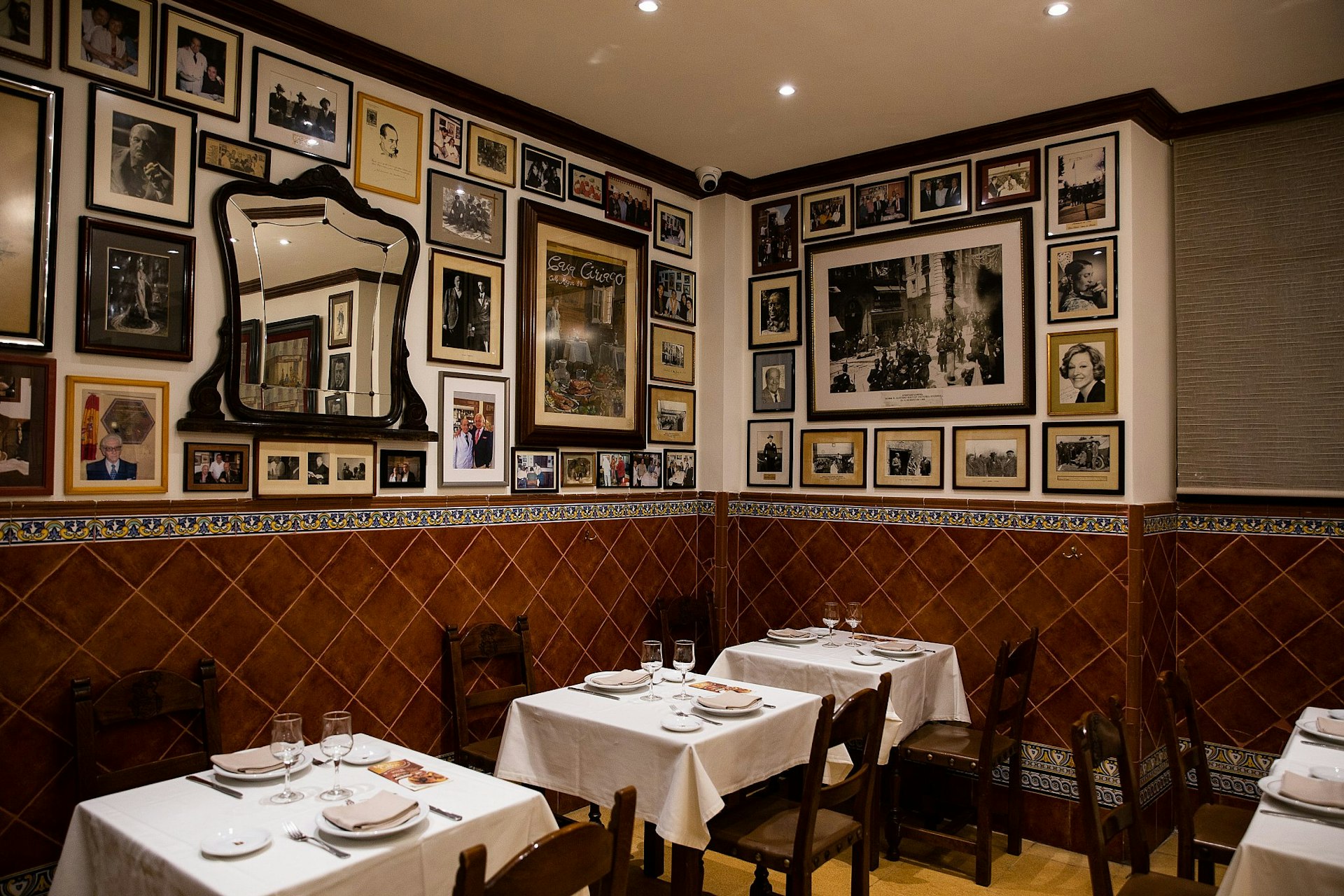 The interior of Casa Ciriaco in Madrid: many historic photos line the walls, and there are dark wood chairs and white tablecloths.