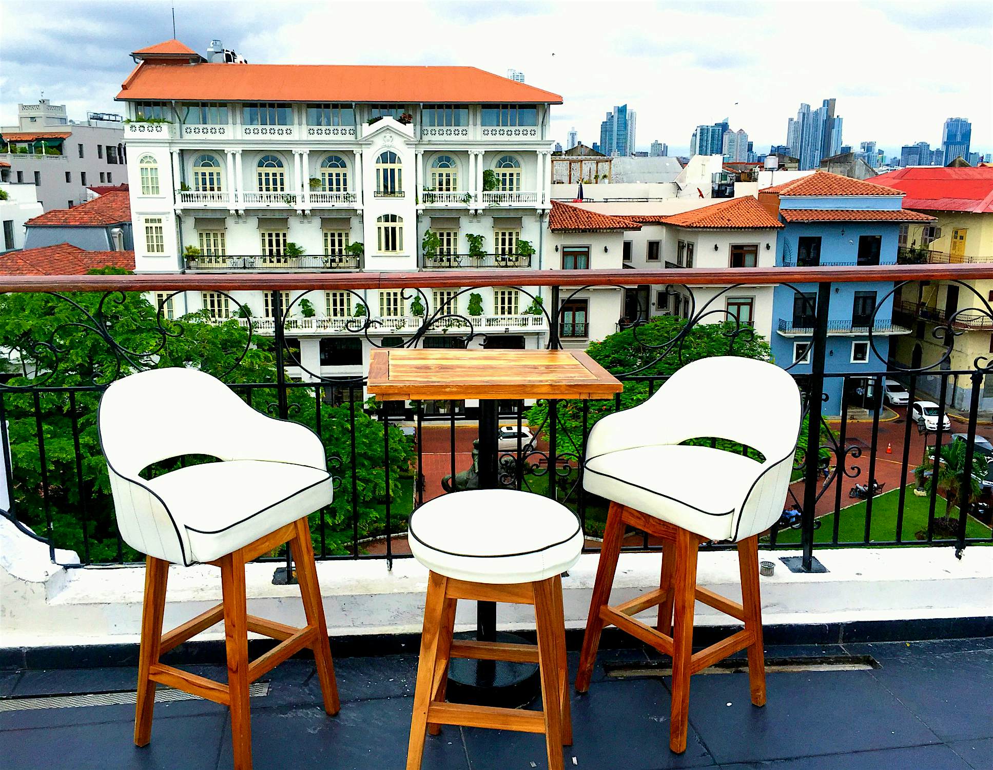 Casa-Casco-rooftop-bar.jpg A pair of white bar chairs and a small table are pushed up against a rail on a rooftop bar in Panama. From this vantage point you can see downtown Casco Viejo.