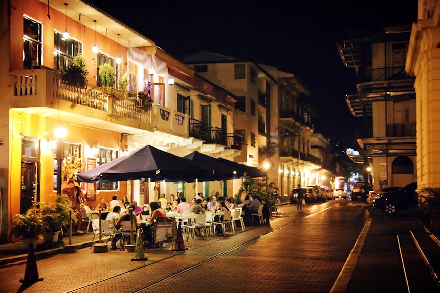 Groups of people sit at tables installed with large umbrellas outside of a restaurant next to cobbled stone streets in the historic Casco Viejo 
