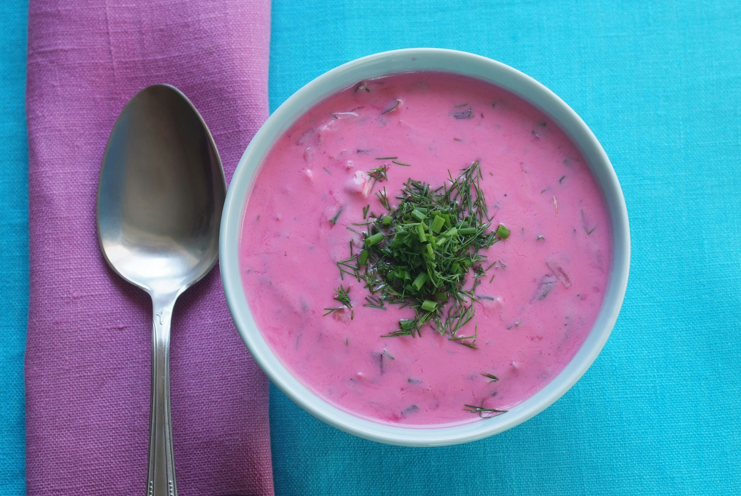 A bowl of bright pink soup, topped with chopped green herbs