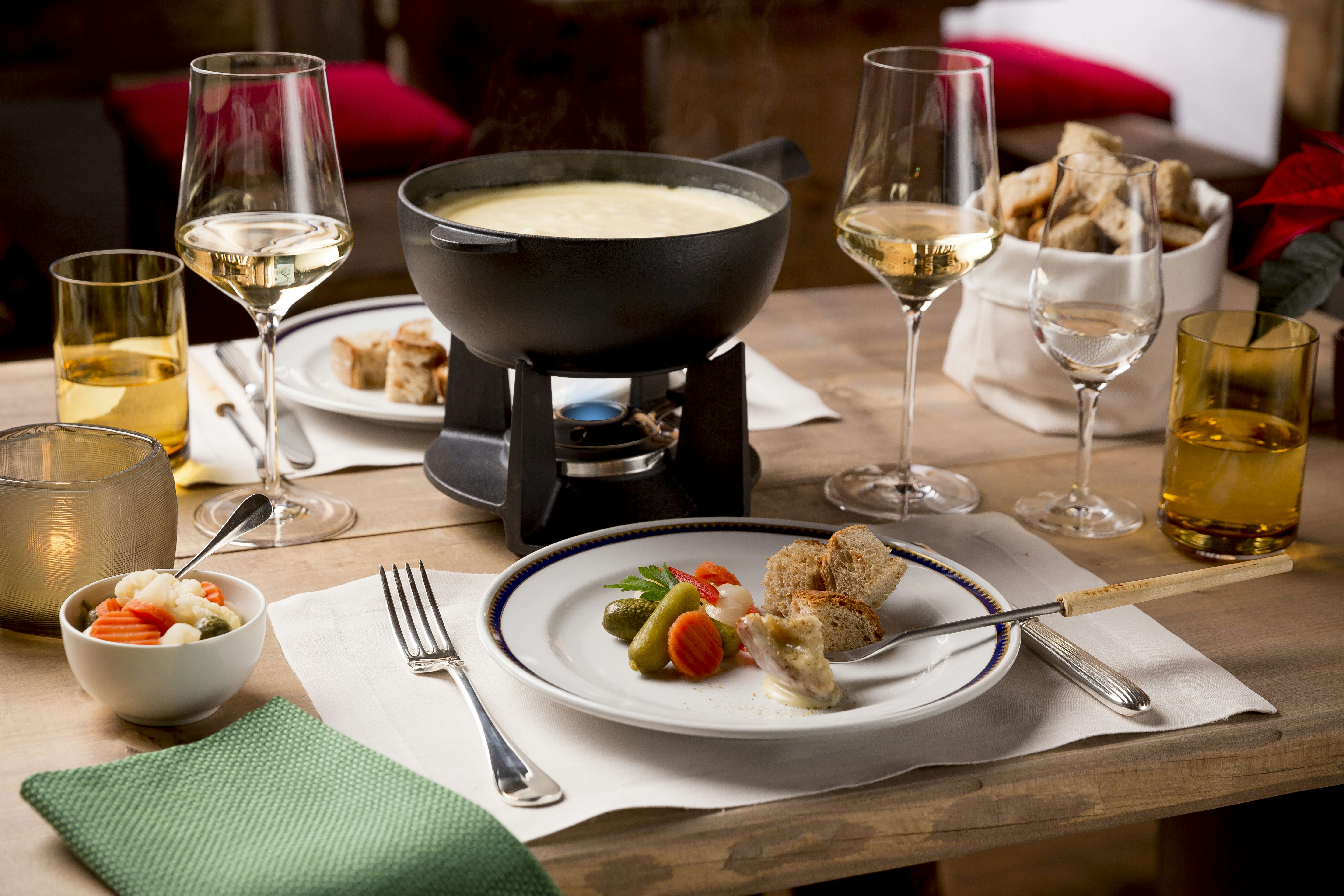 A table is laid with a cheese fondue, bread, vegetables, and glasses of white wine at Baur au Lac's Chalet au Lac.