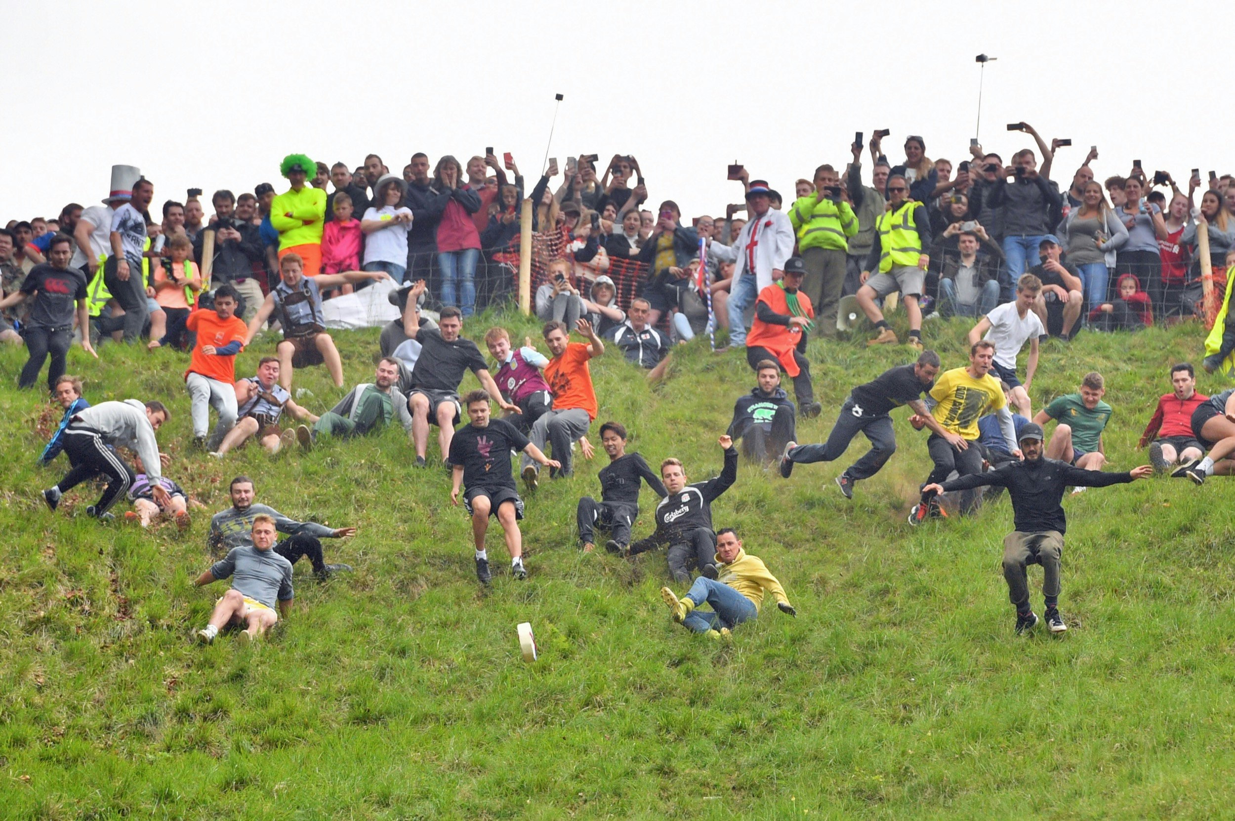 Competitors throw themselves down a steep hill in England in a race to the bottom behind a rolling wheel of cheese; Unique sporting events